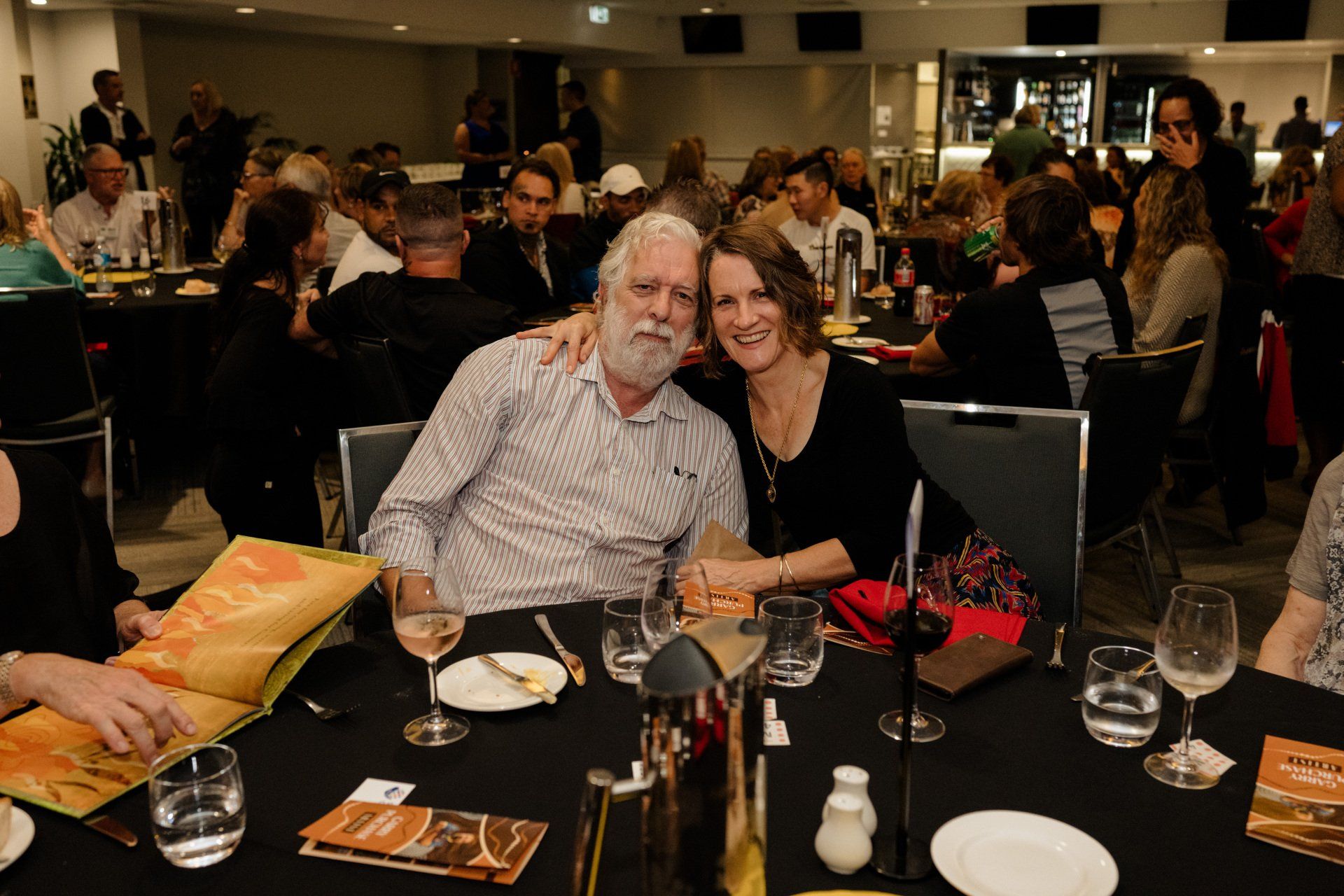 A man and a woman are posing for a picture at a table in a restaurant.
