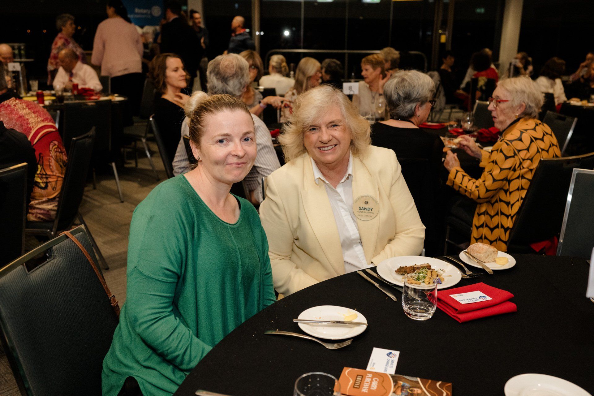 Two women are sitting at a table with plates of food.