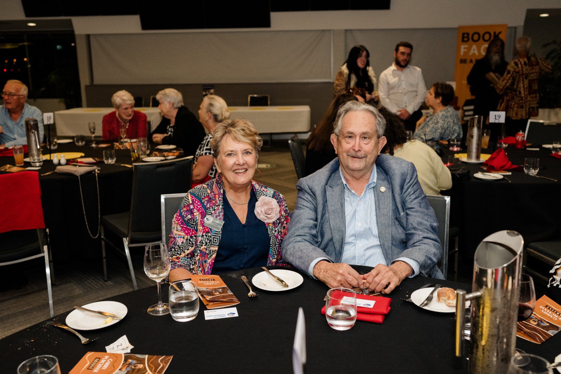 A man and a woman are sitting at a table with plates and glasses of wine.
