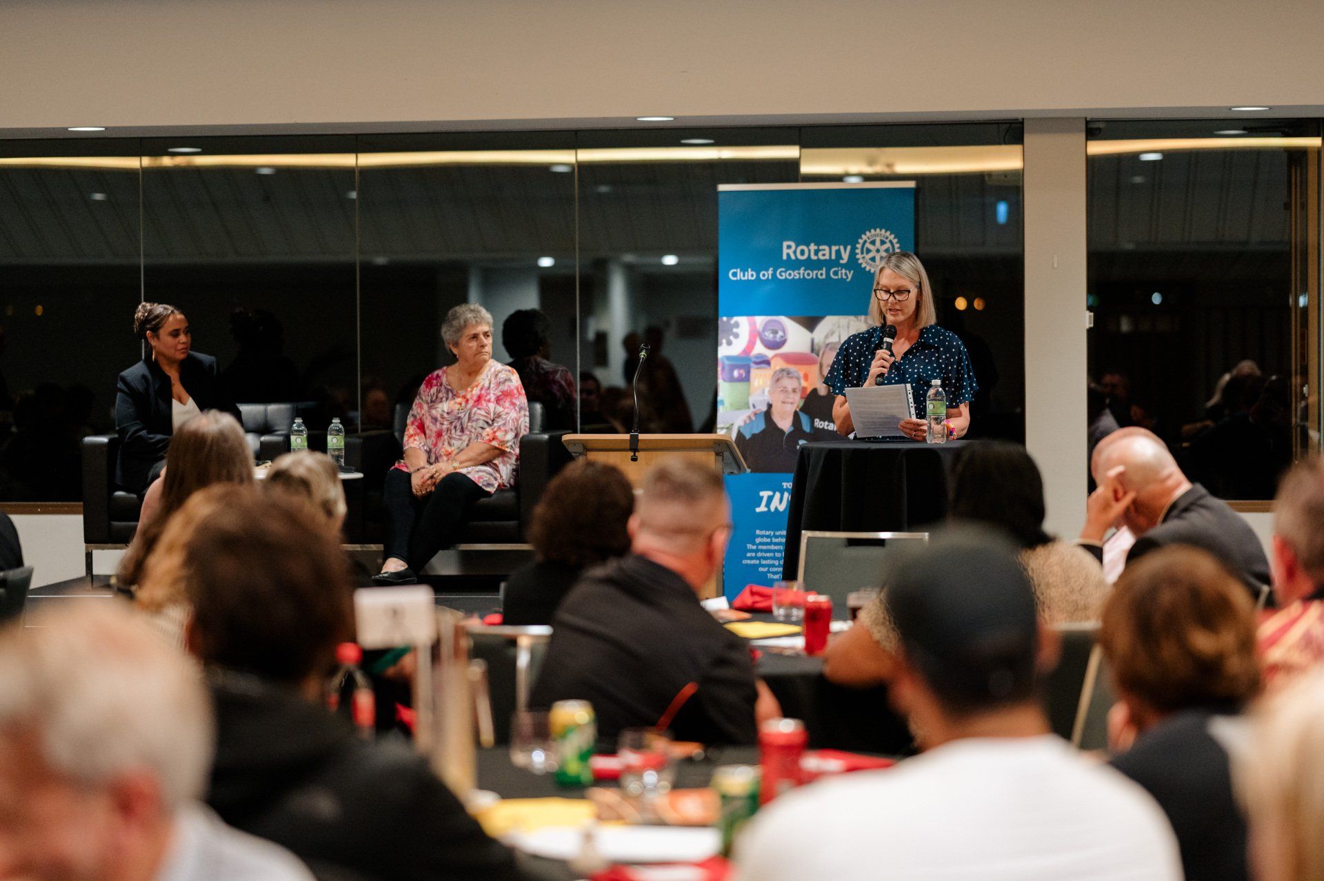 A woman is giving a speech to a crowd of people sitting at tables.