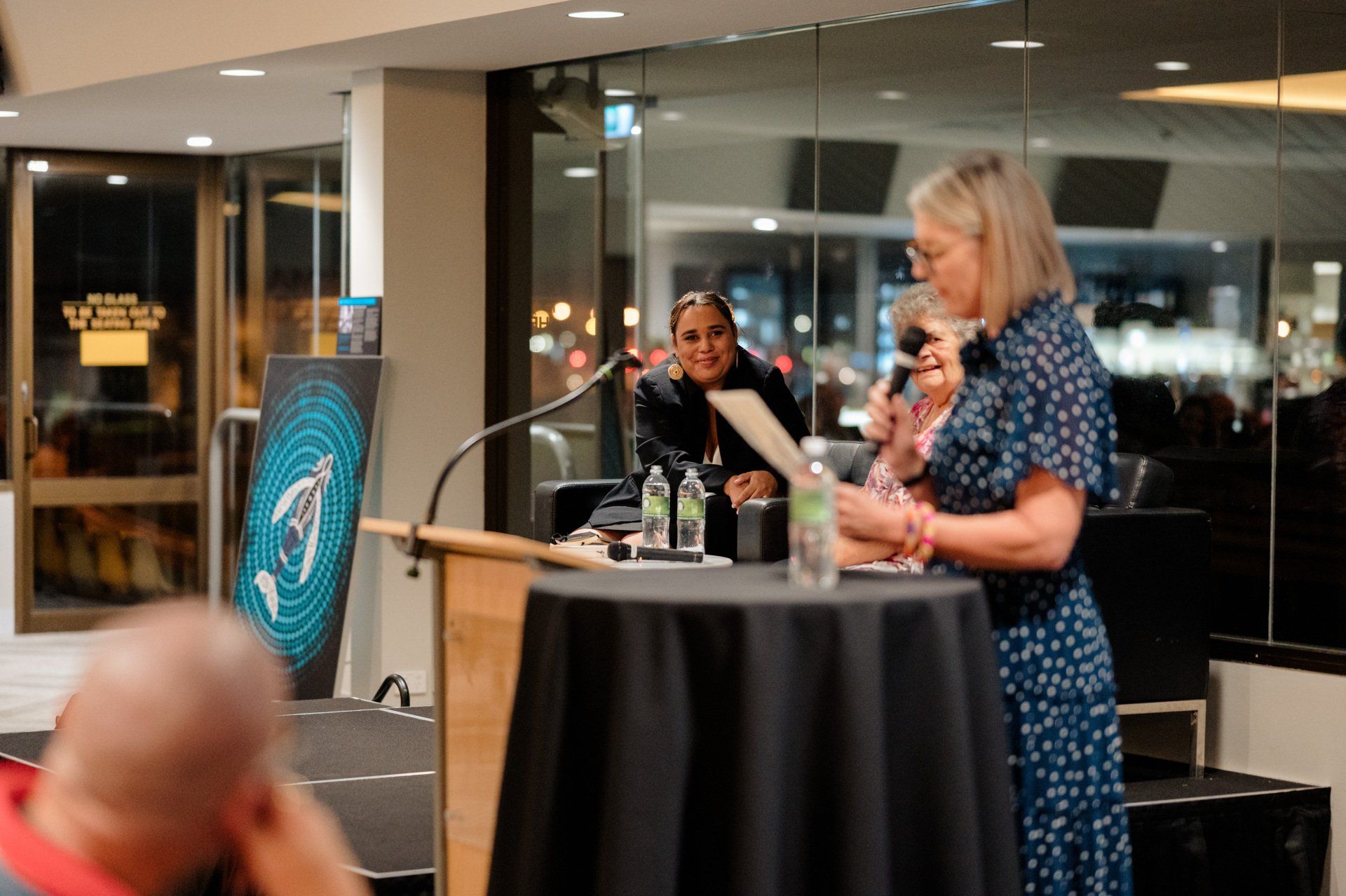 A woman is standing at a podium speaking into a microphone.