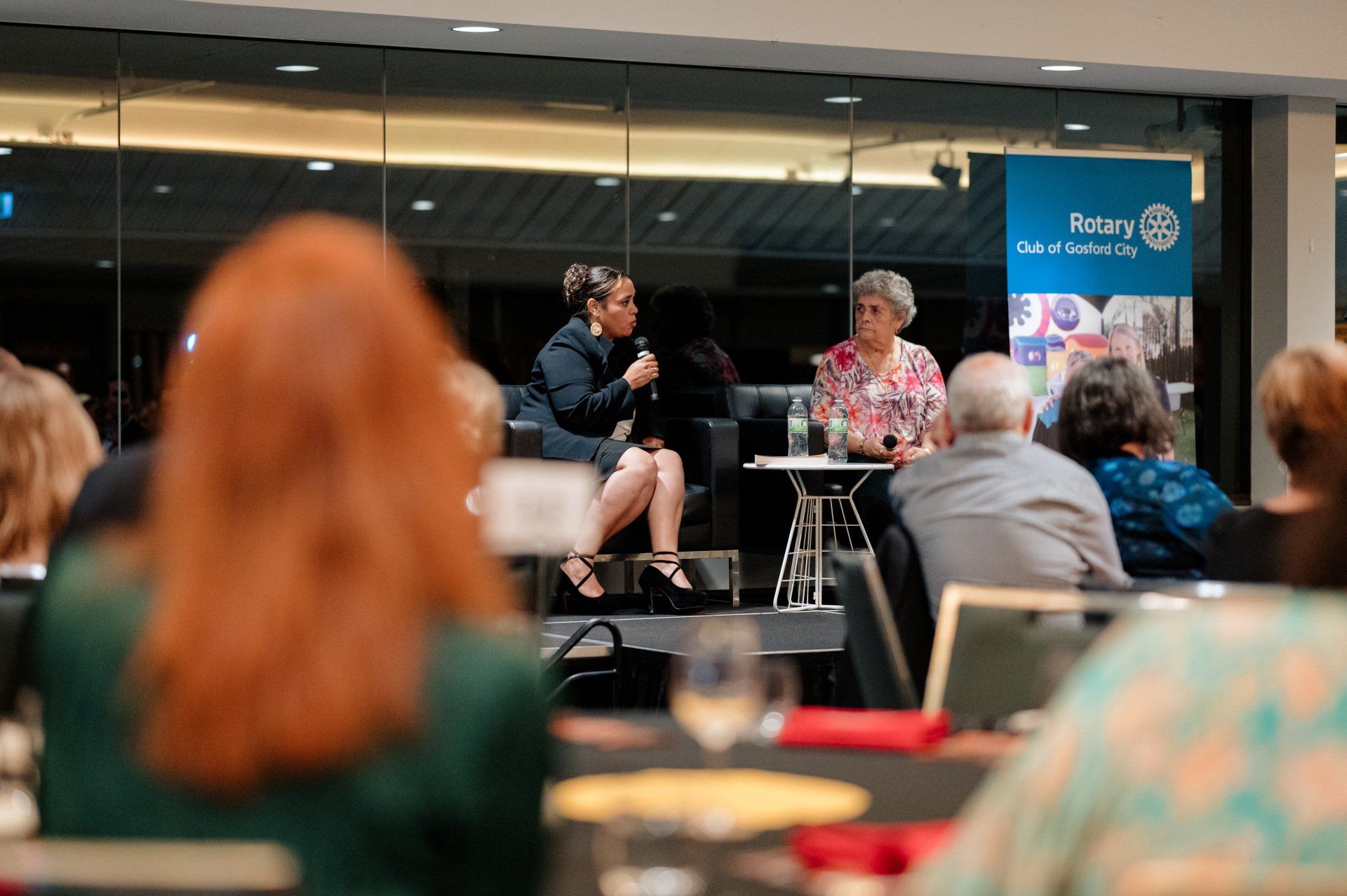 A woman is sitting on a stage talking to a group of people.