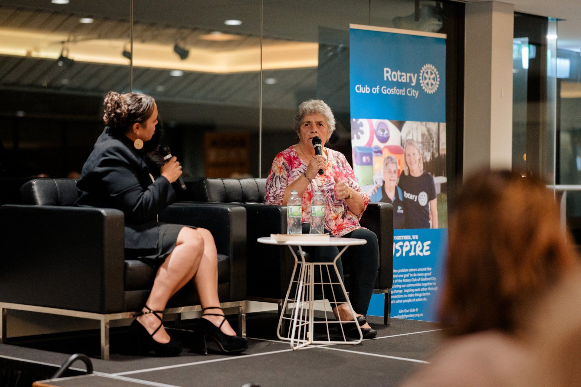 Two women are sitting in chairs talking into microphones.
