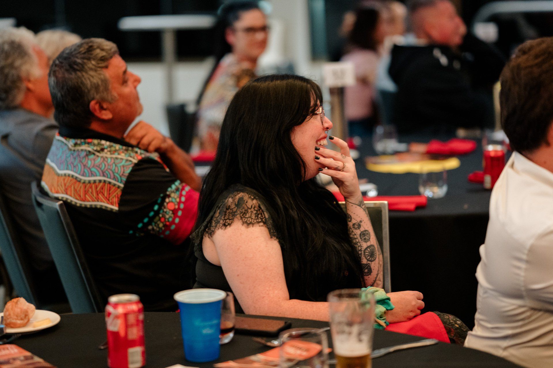A woman is sitting at a table with a glass of beer and a can of soda.