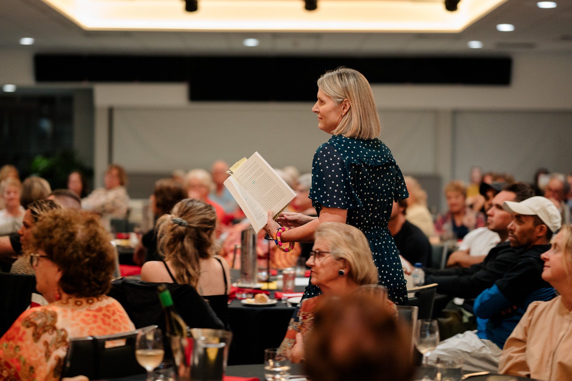 A woman is standing in front of a crowd of people holding a book.