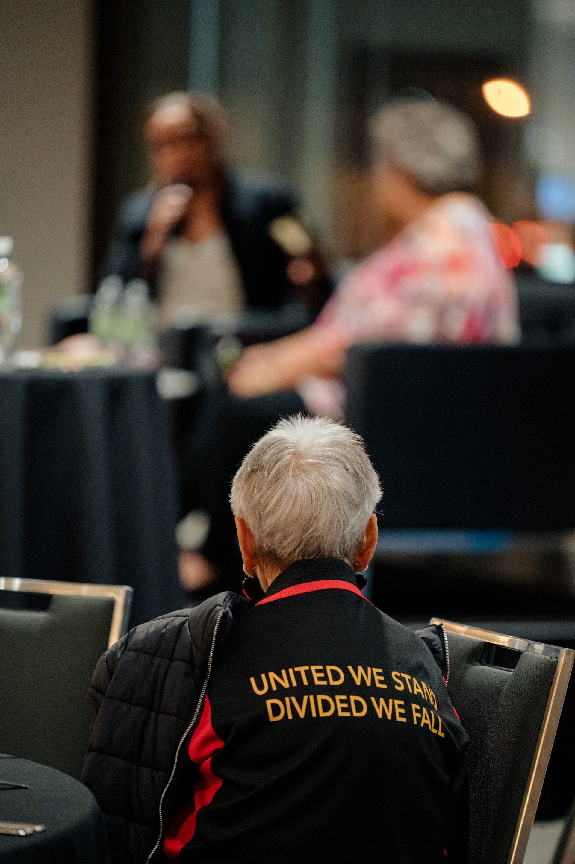 A man wearing a jacket that says `` united we stand divided we fall '' is sitting in a chair.