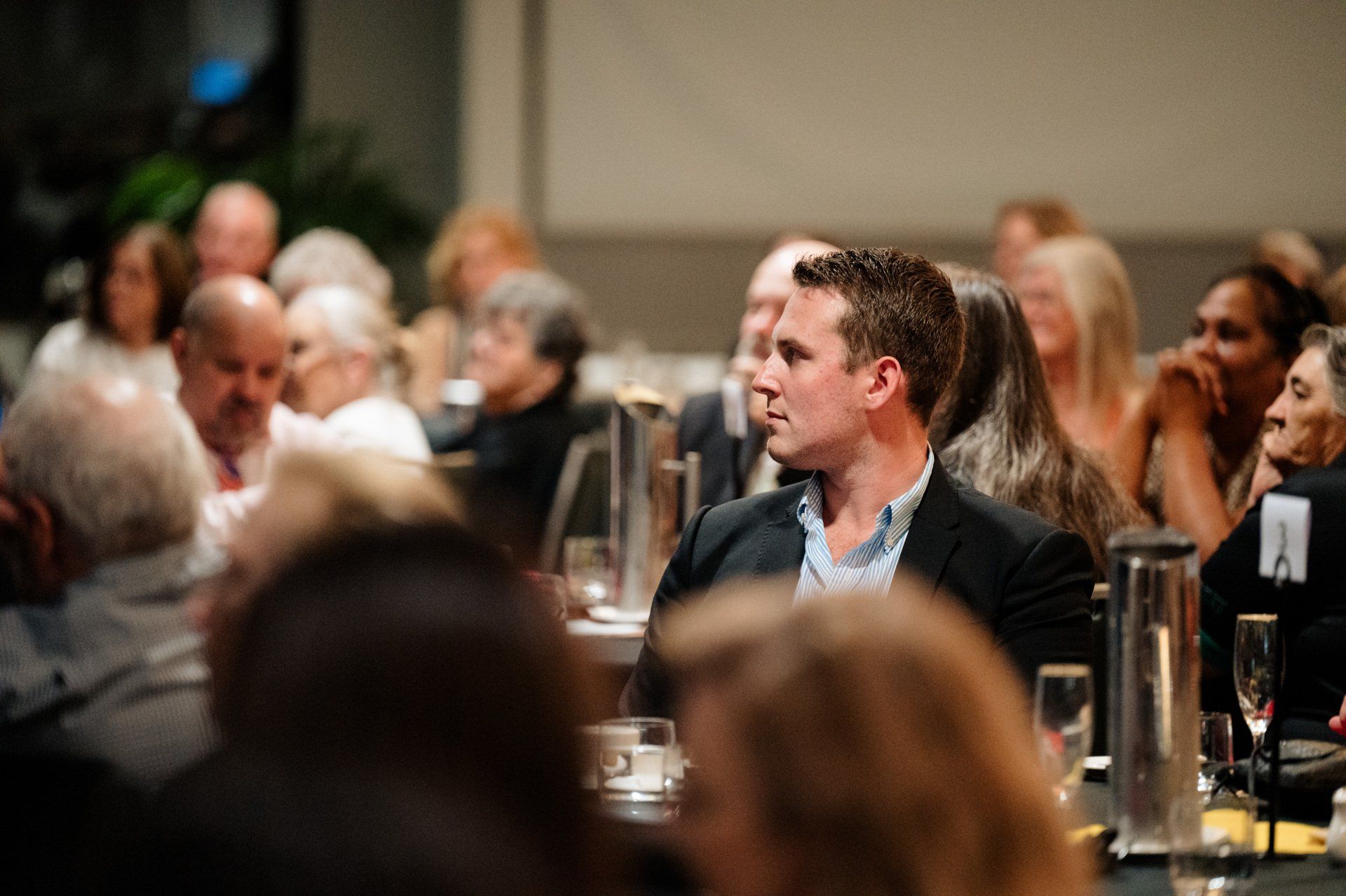 A man is sitting at a table in front of a crowd of people.