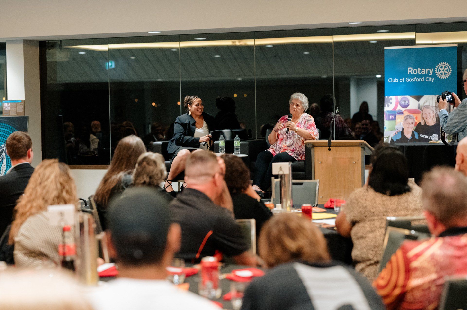 A group of people are sitting at tables in front of a podium.