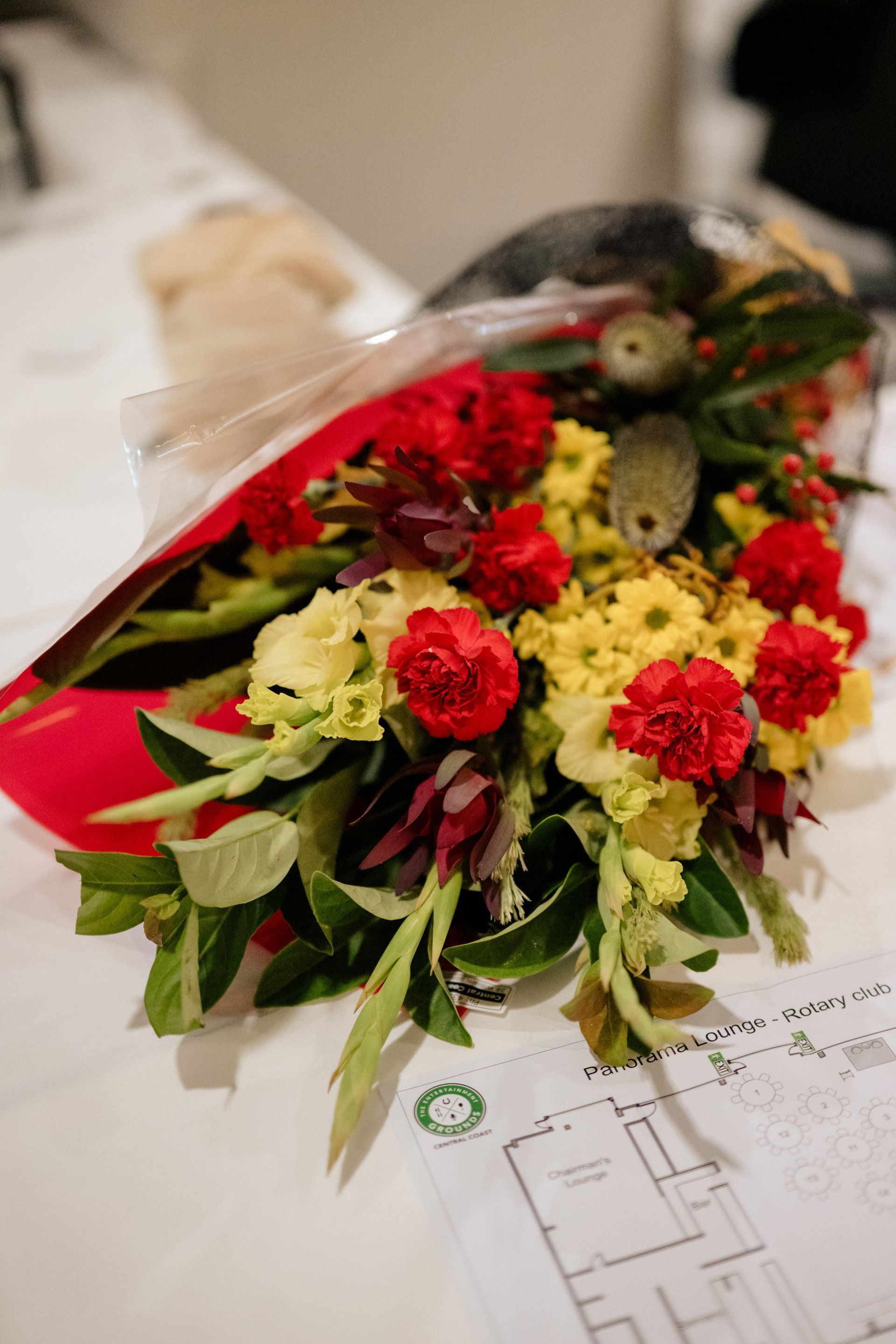 A bouquet of red and yellow flowers is sitting on a table next to a blueprint.