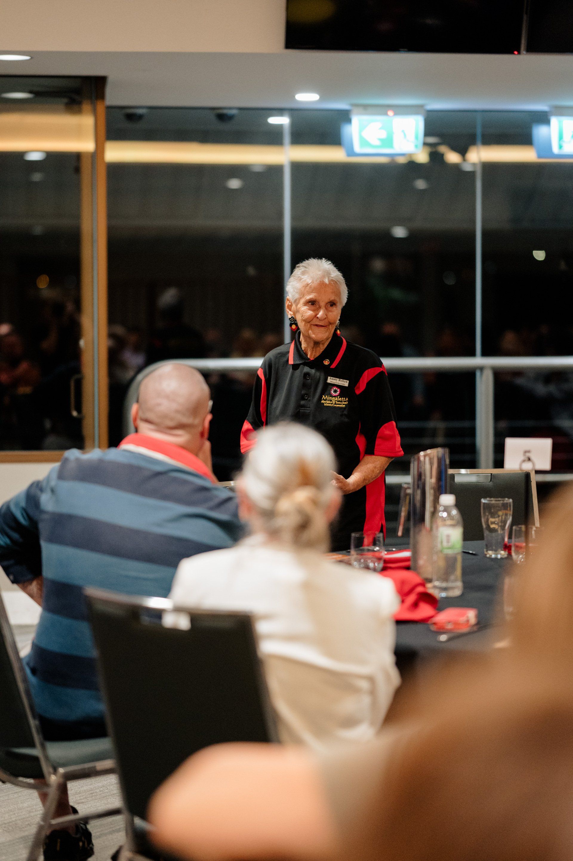 A woman is standing in front of a group of people sitting at a table.