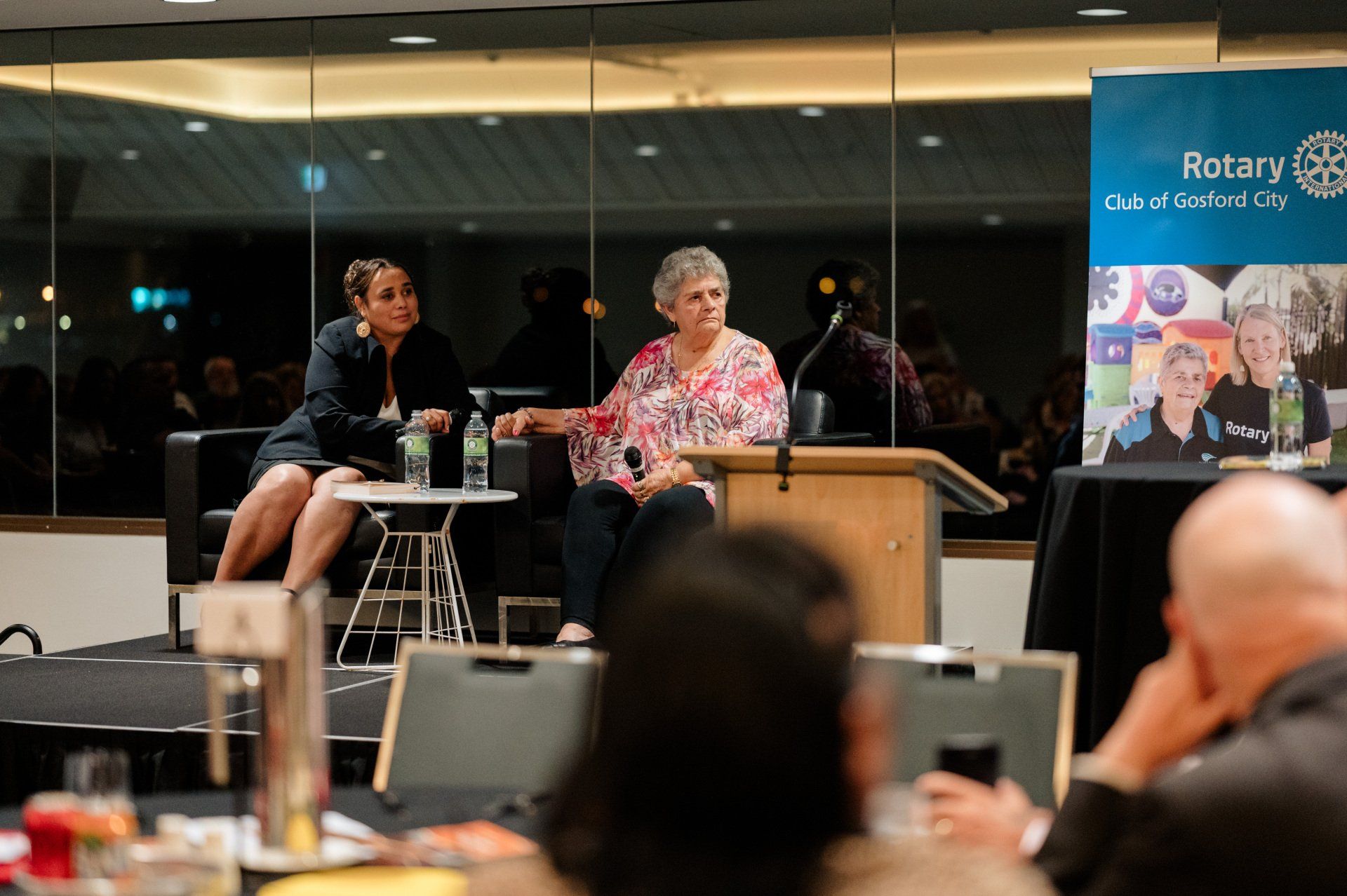 A woman is giving a speech at a podium in front of a group of people.