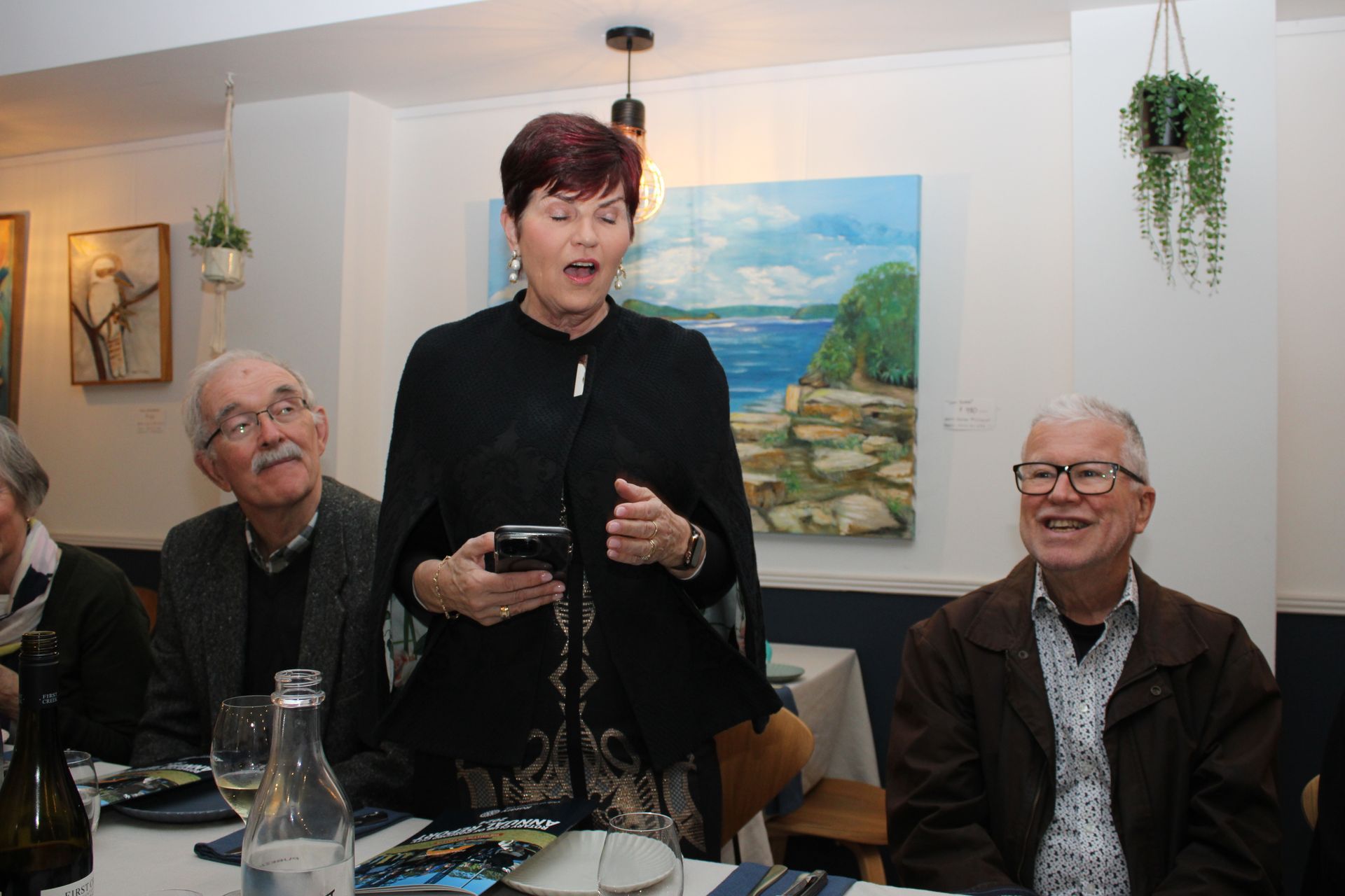 A woman is standing in a restaurant talking to a group of people.