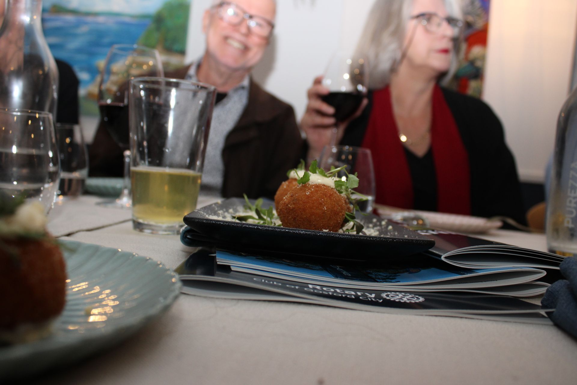 A man and woman are sitting at a table with plates of food and glasses of wine.