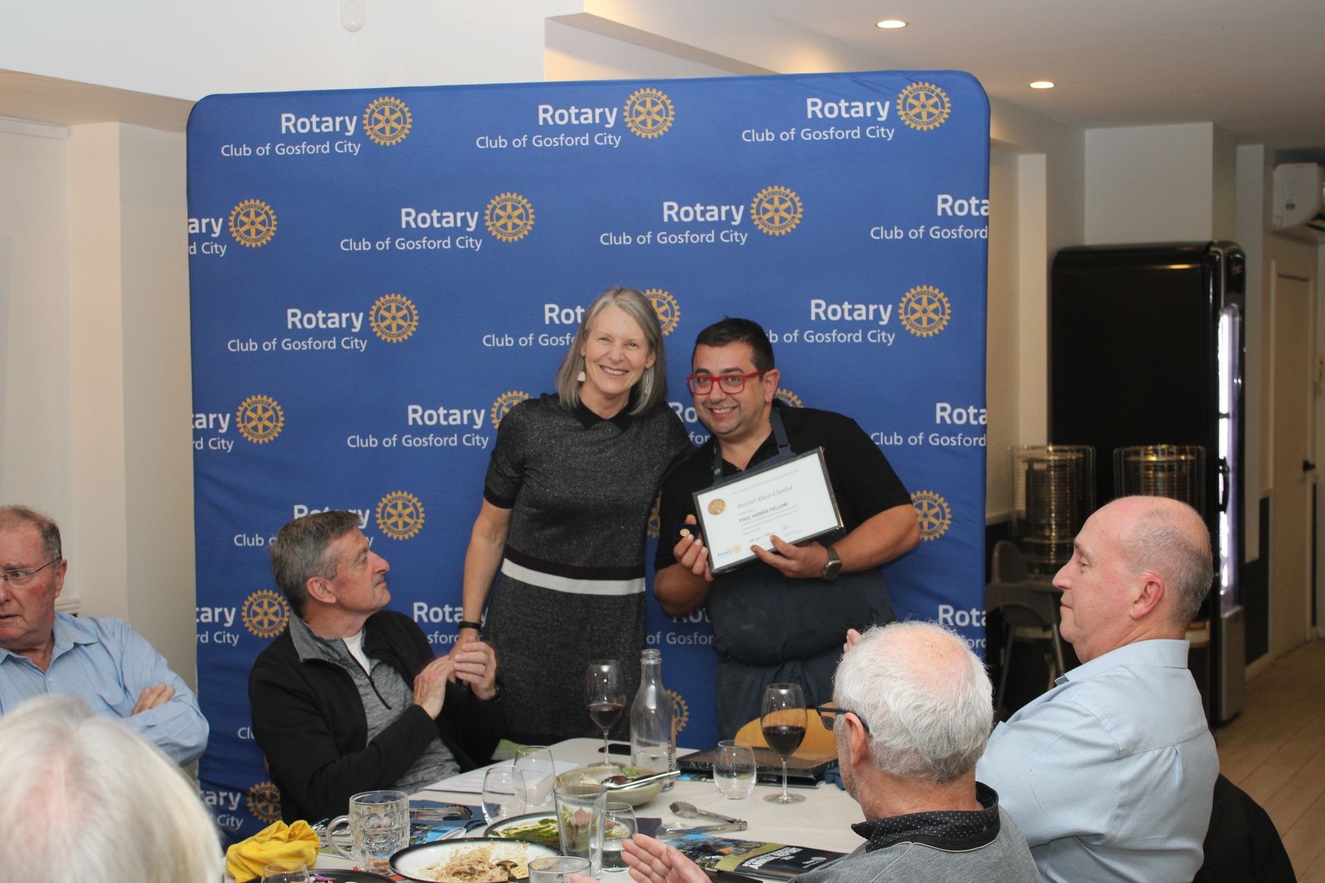 A group of people are sitting around a table holding a certificate.