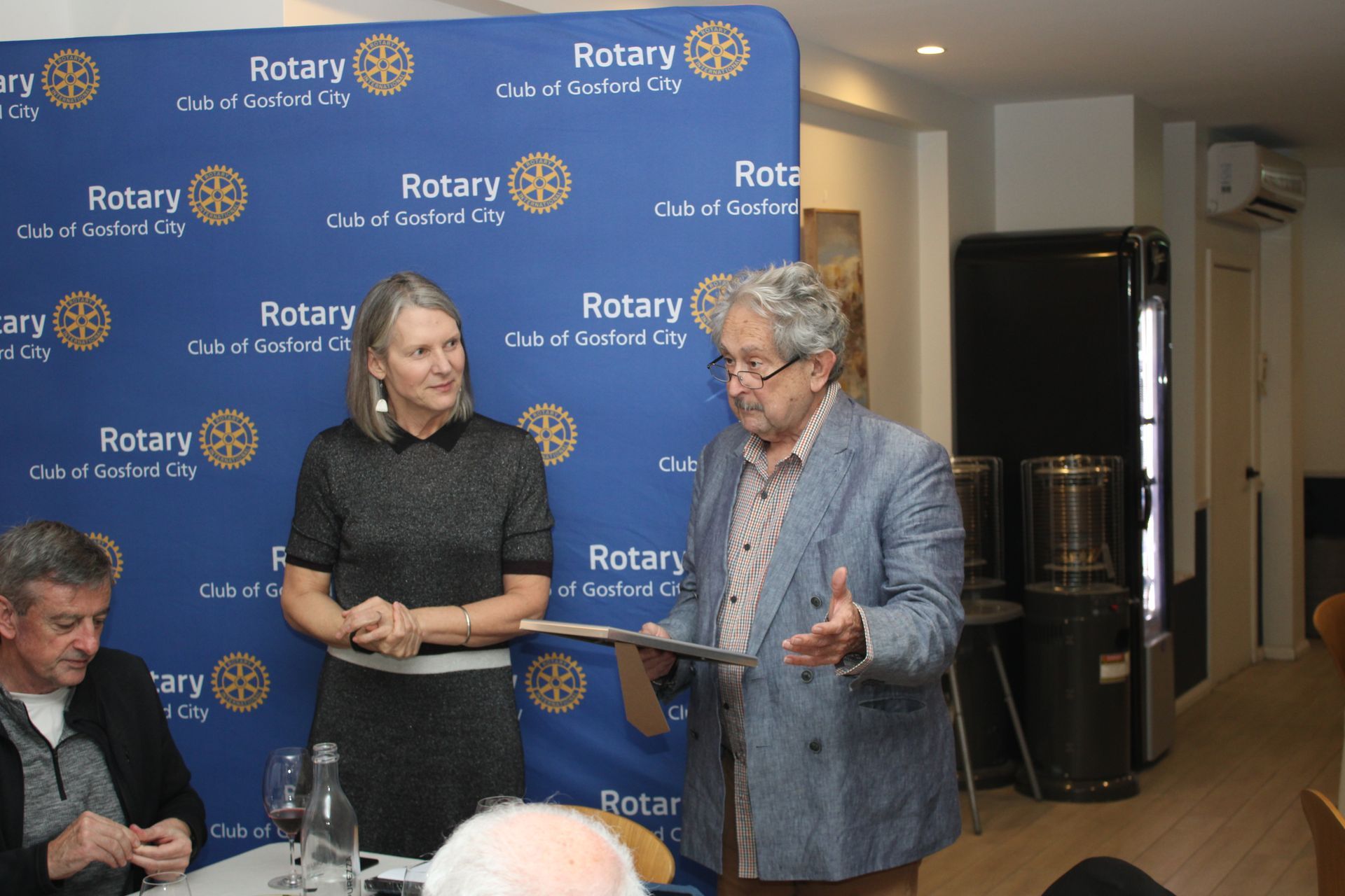 A man and a woman are standing next to each other in front of a rotary sign.