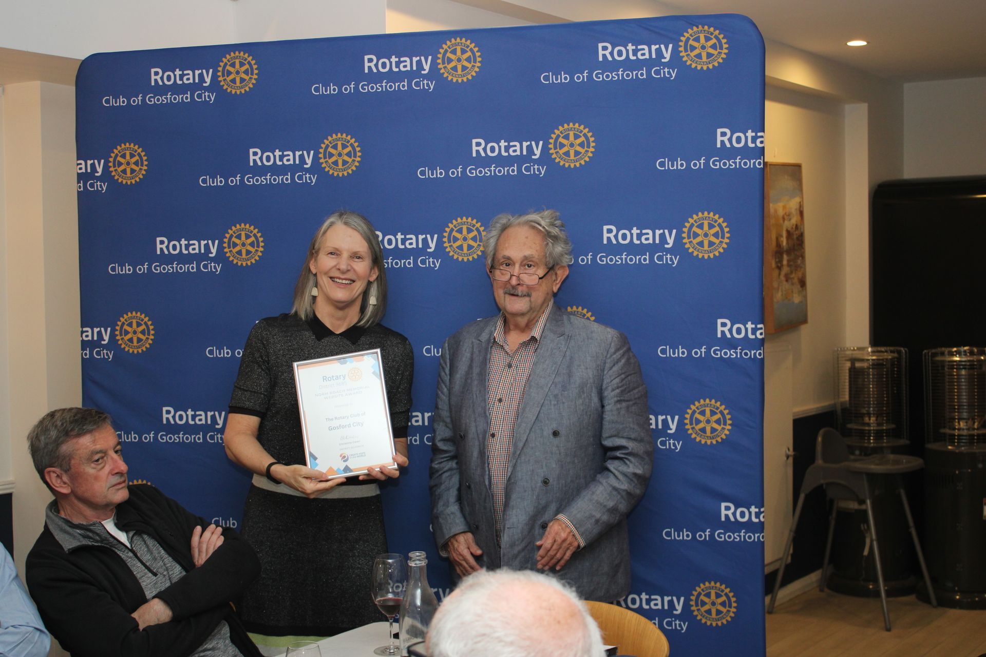 A woman is holding a certificate in front of a group of people.