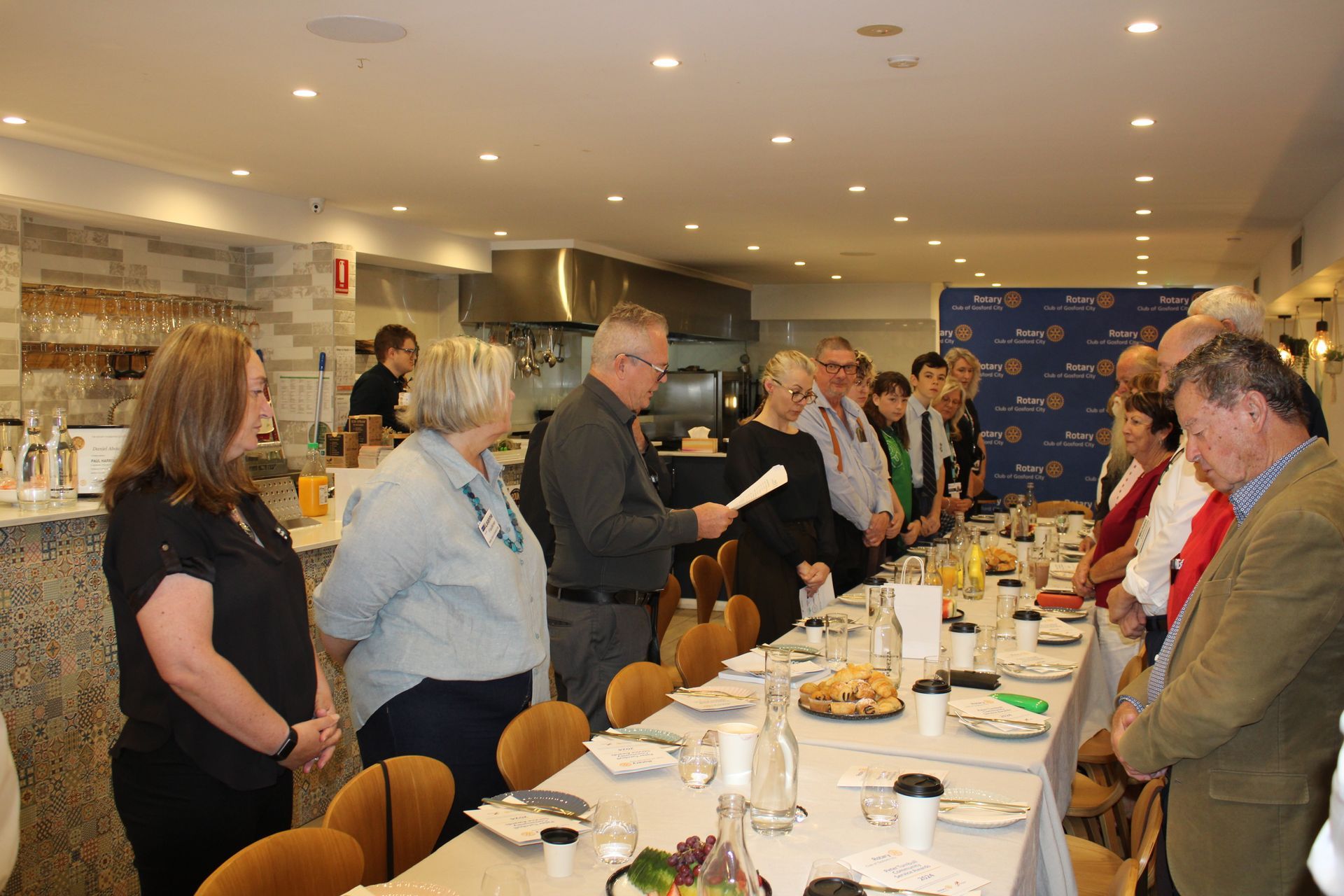 A group of people are standing around a long table in a restaurant.