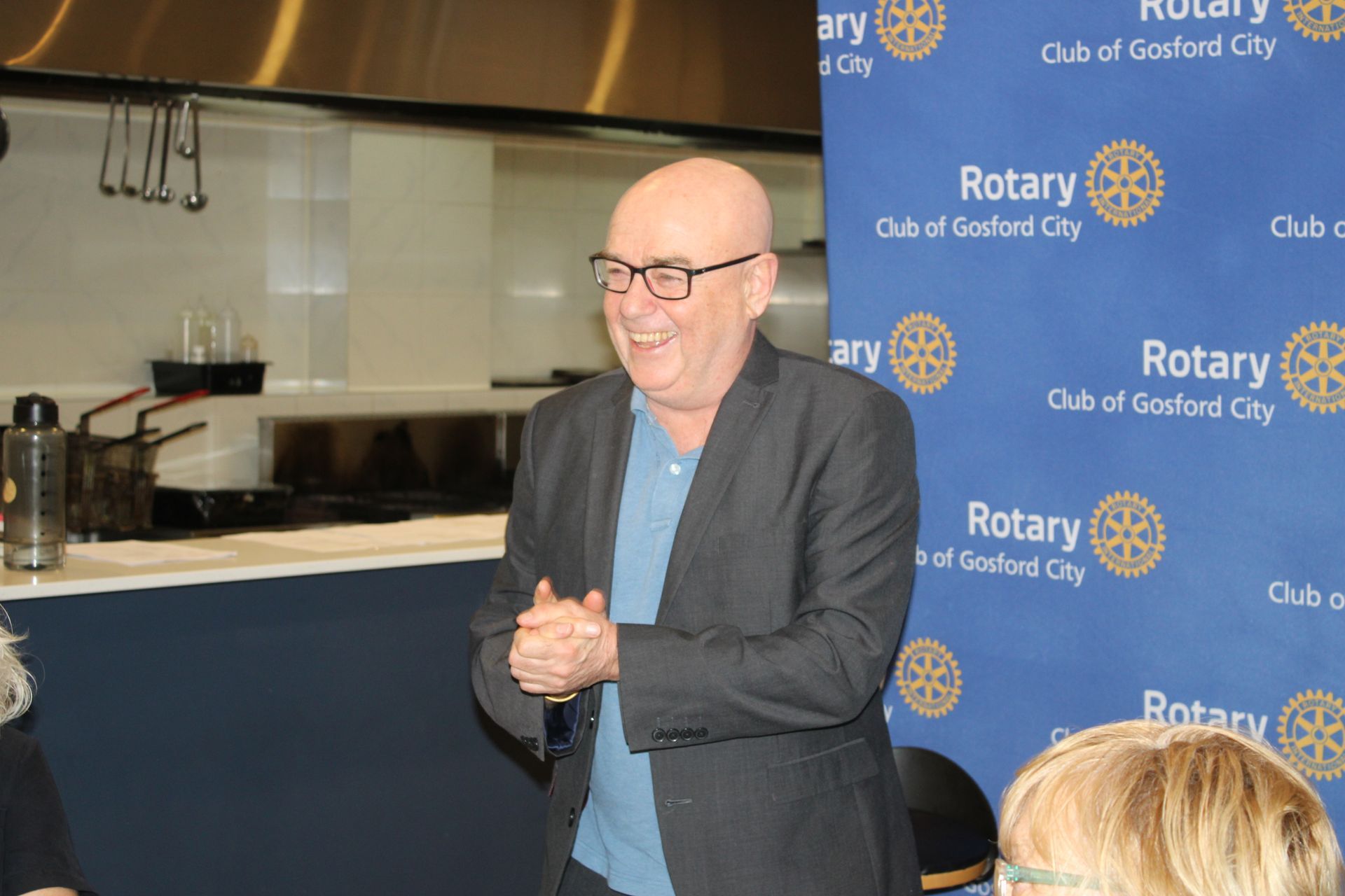 A man in a suit and glasses is standing in front of a rotary sign.