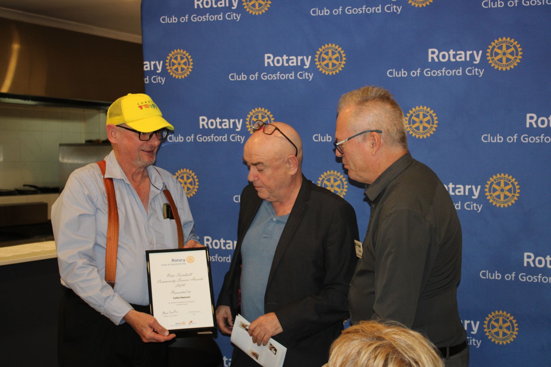 Three men are standing in front of a blue wall that says rotary
