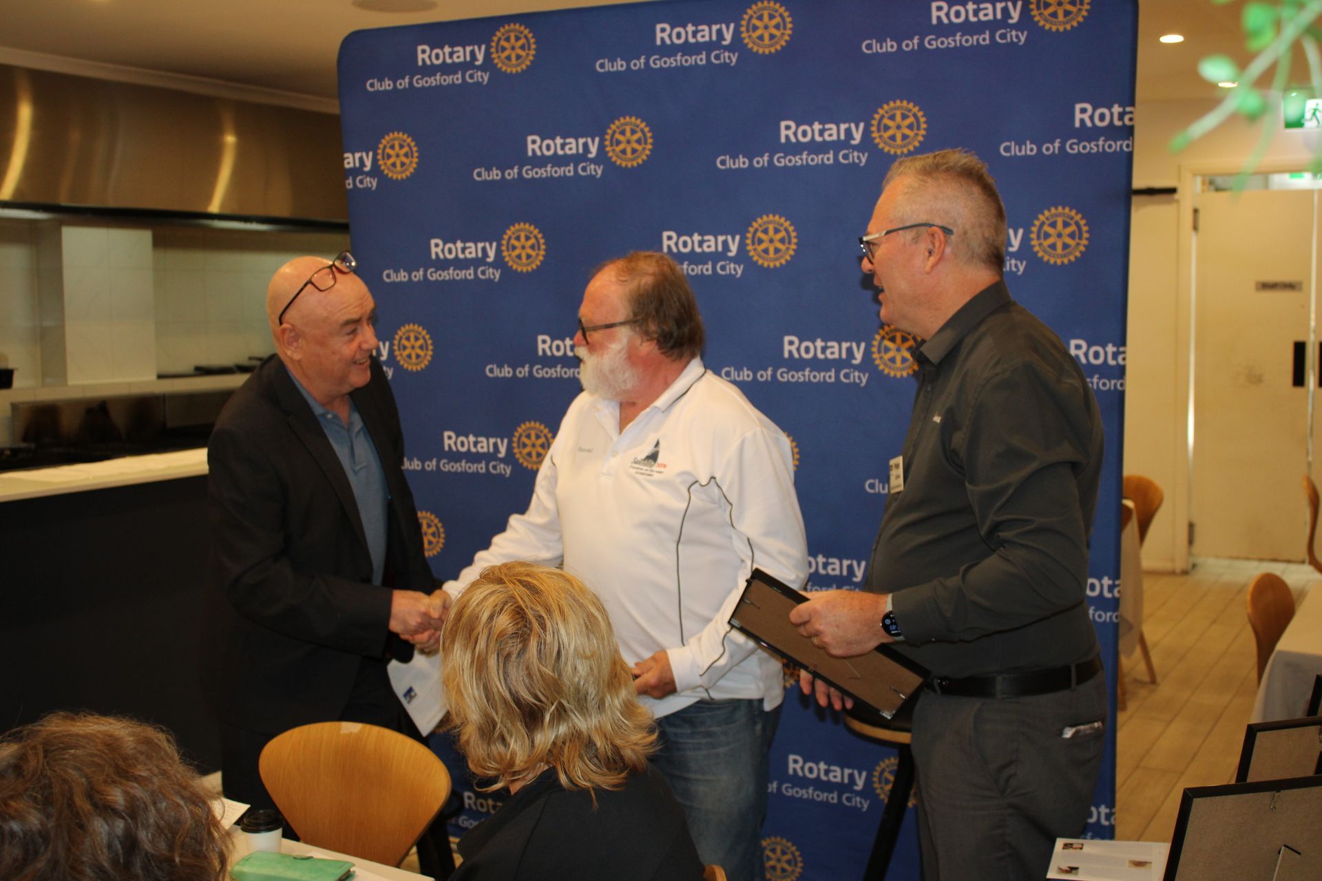 A group of people are shaking hands in front of a blue wall that says rotary