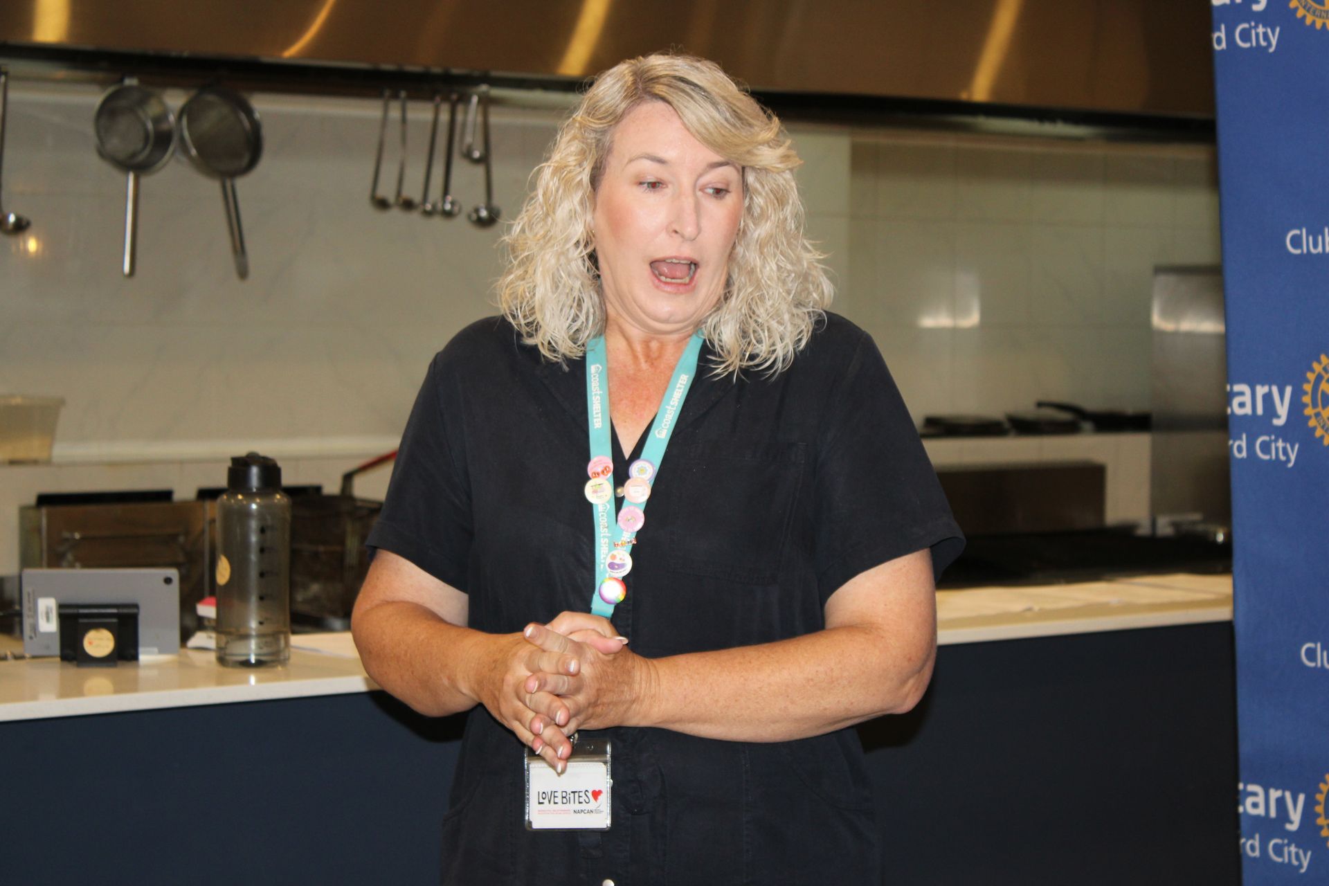 A woman in a black shirt is standing in a kitchen talking to someone.