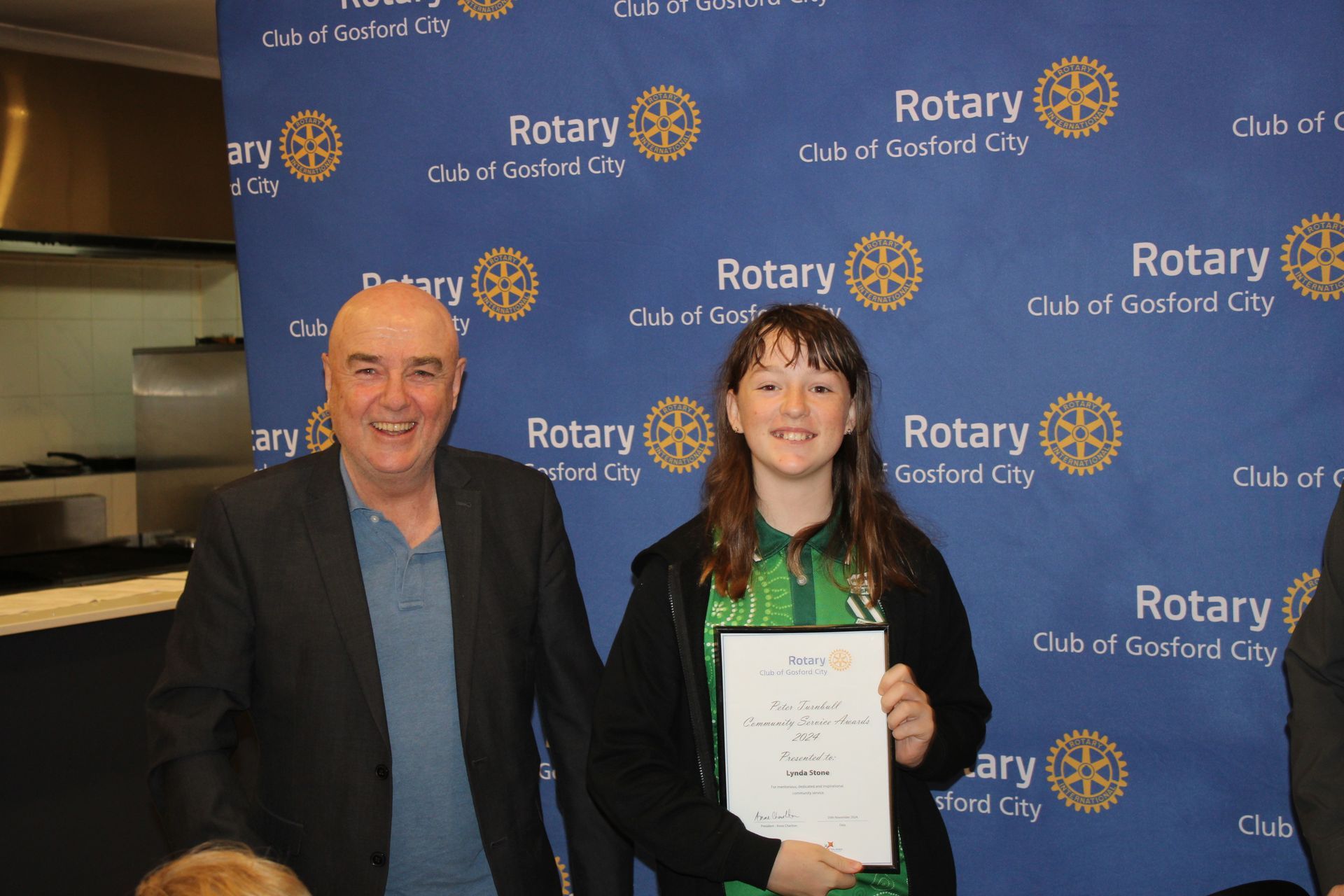 A man and a girl are posing for a picture in front of a rotary sign.