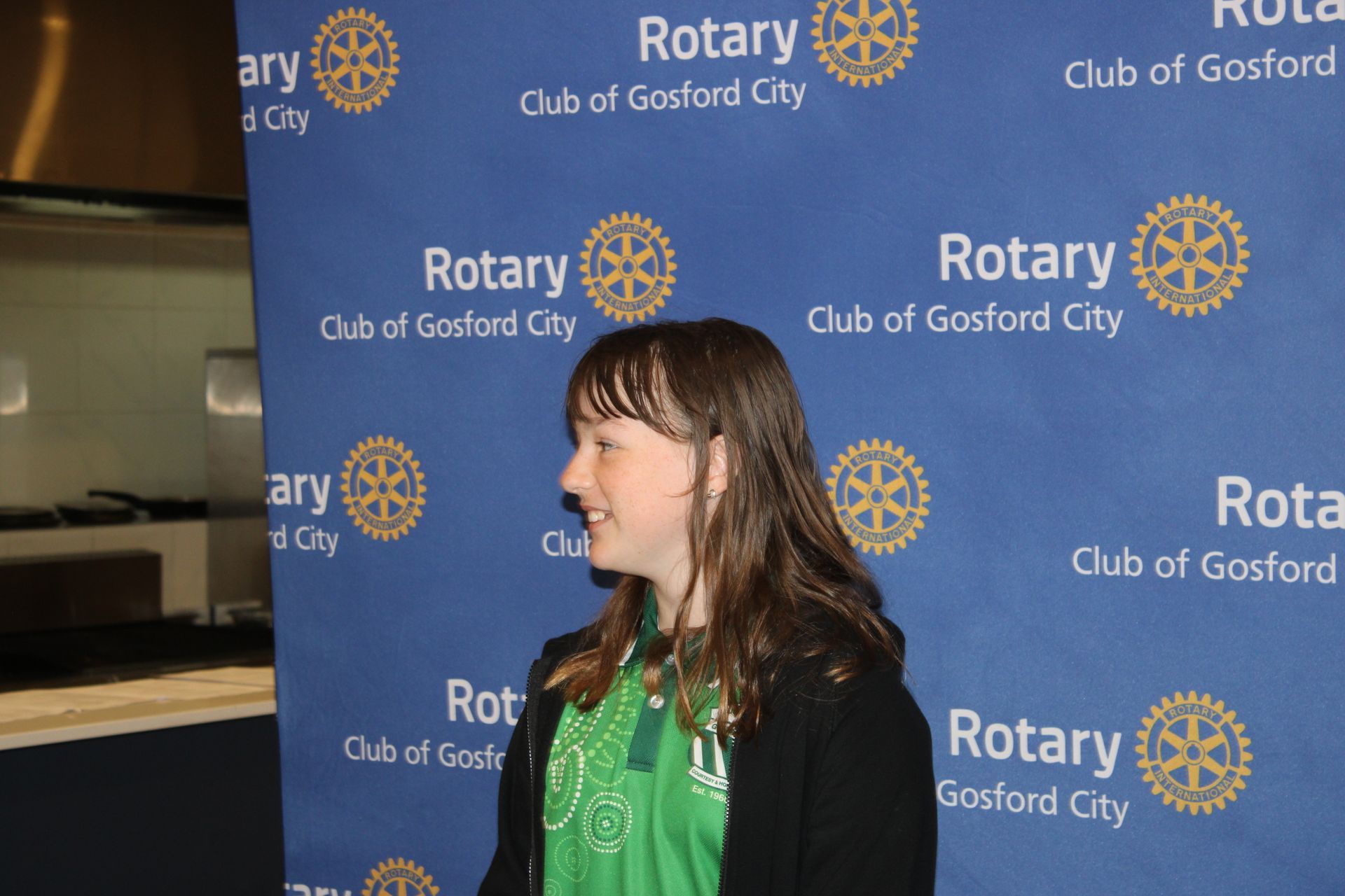 A girl stands in front of a blue background that says rotary
