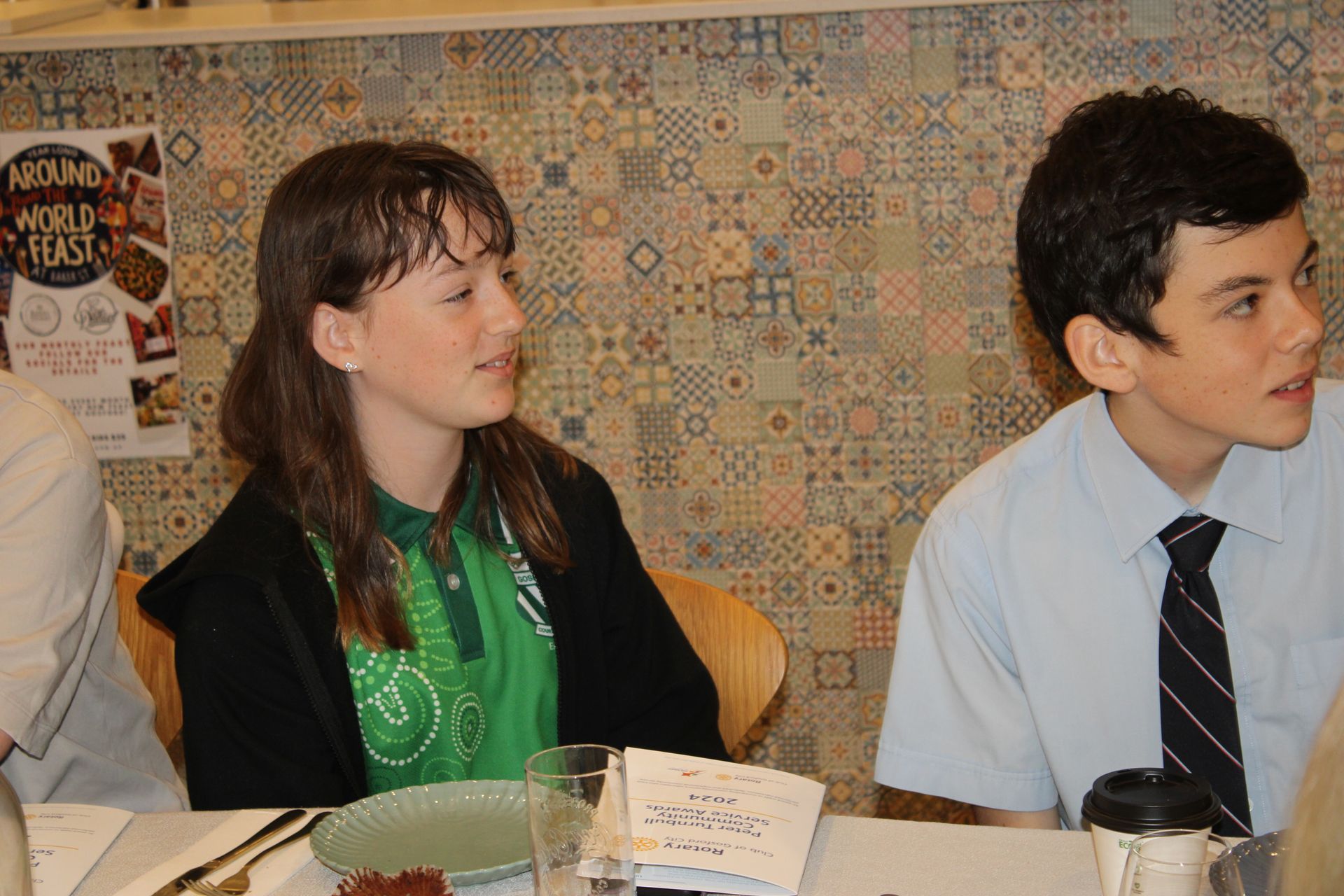 A boy and a girl are sitting at a table with a poster on the wall that says around world toast