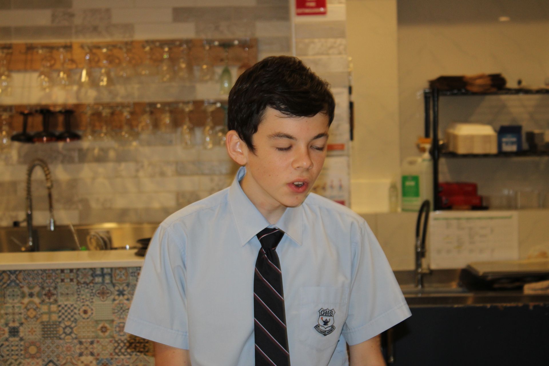A young boy wearing a shirt and tie is standing in a kitchen.