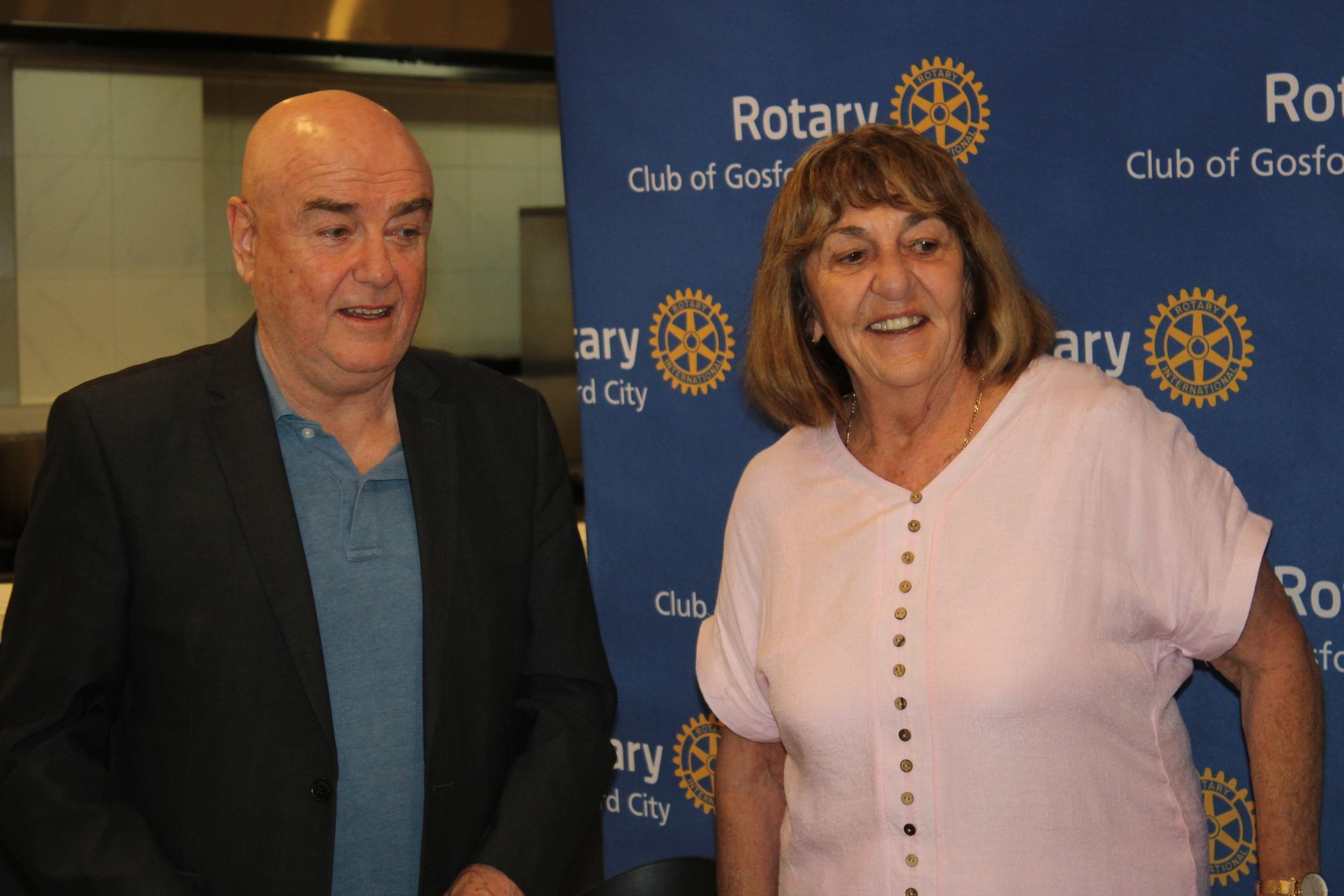 A man and a woman are standing in front of a banner that says rotary