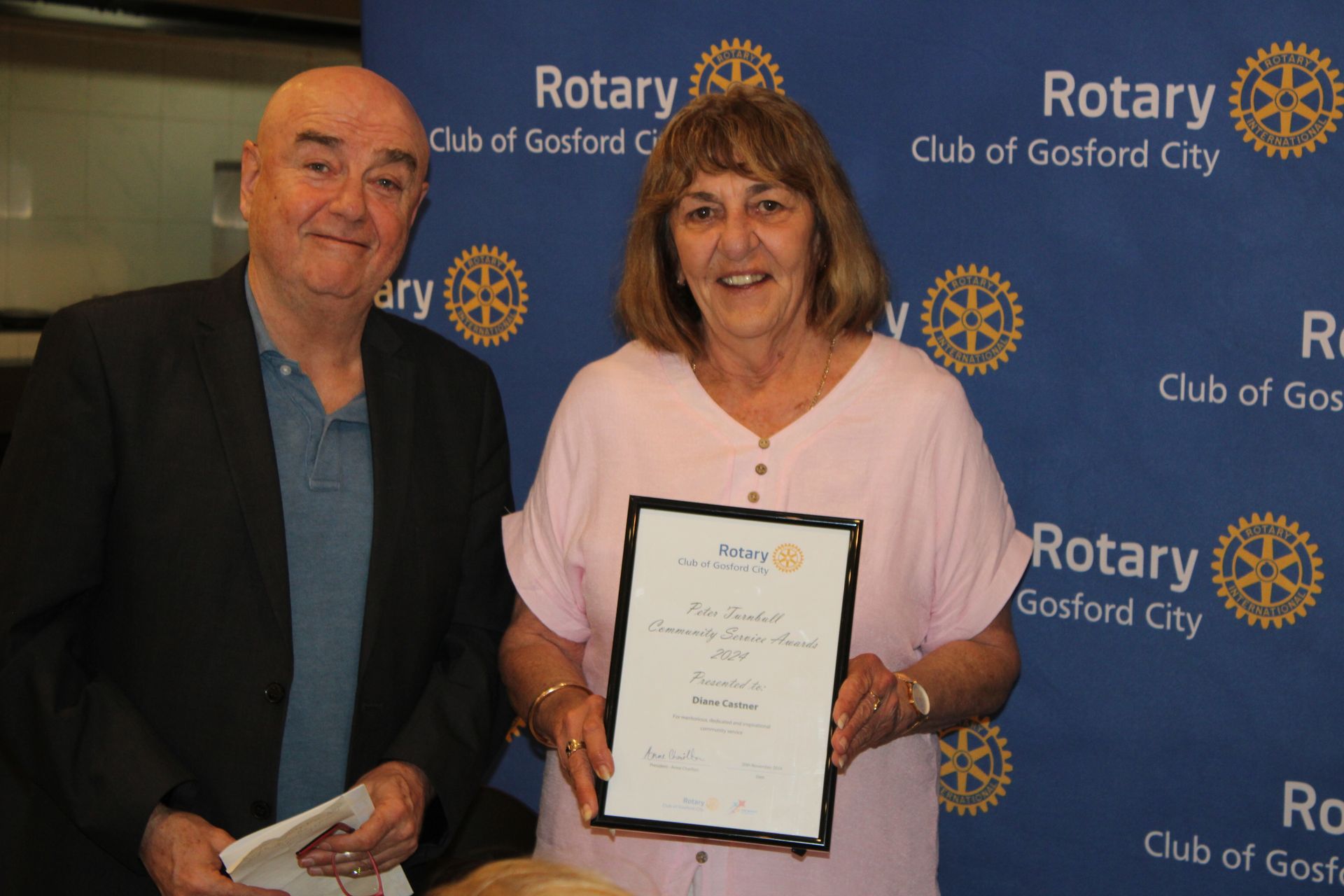 A man and a woman are holding a certificate in front of a sign that says rotary