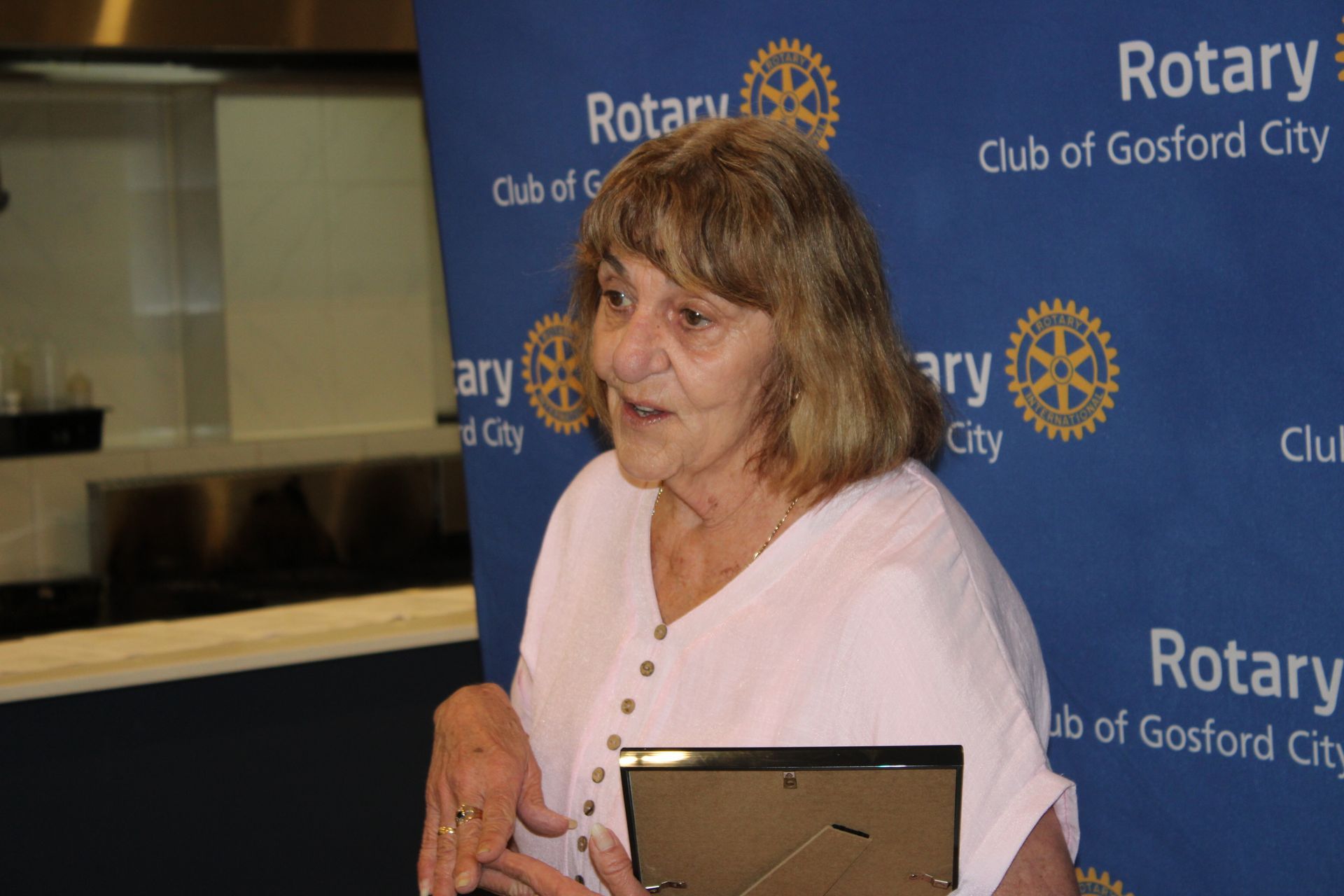 A woman is holding a picture frame in front of a rotary sign.
