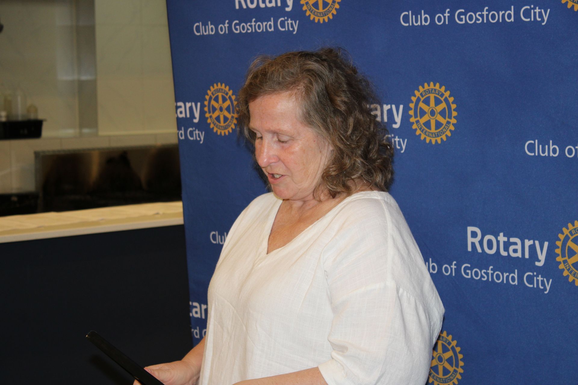 A woman is standing in front of a blue background that says rotary club of gosford city