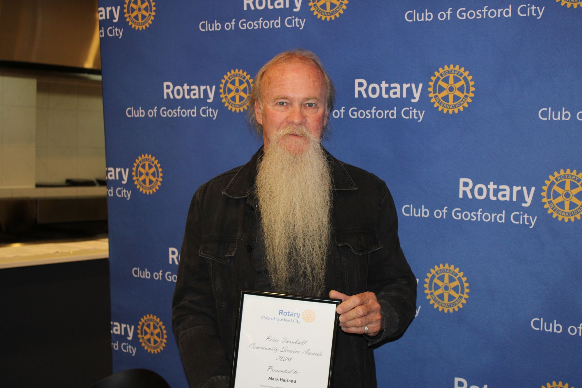 A man with a beard is holding a certificate in front of a blue background that says rotary