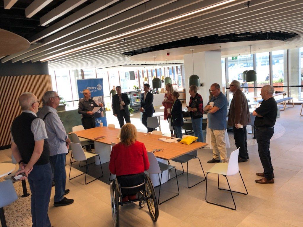 A group of people are standing around a table with a woman in a wheelchair.