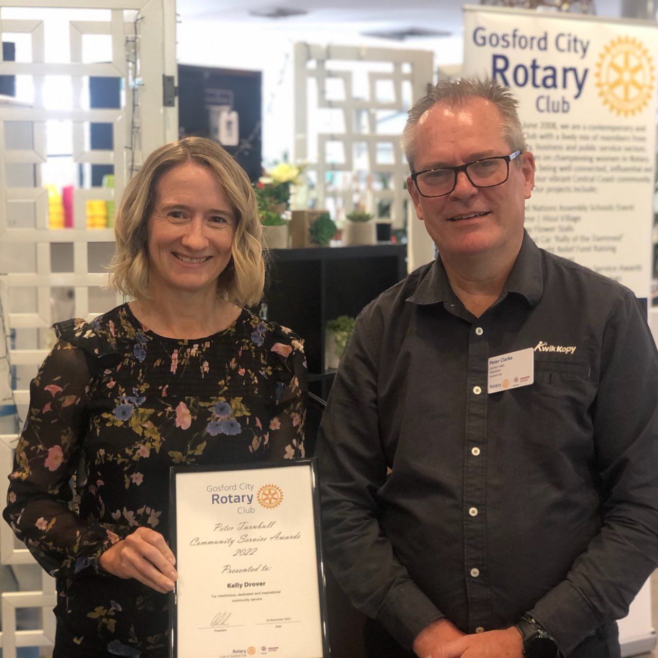 A man and a woman are posing for a picture in front of a sign that says gosford city rotary club