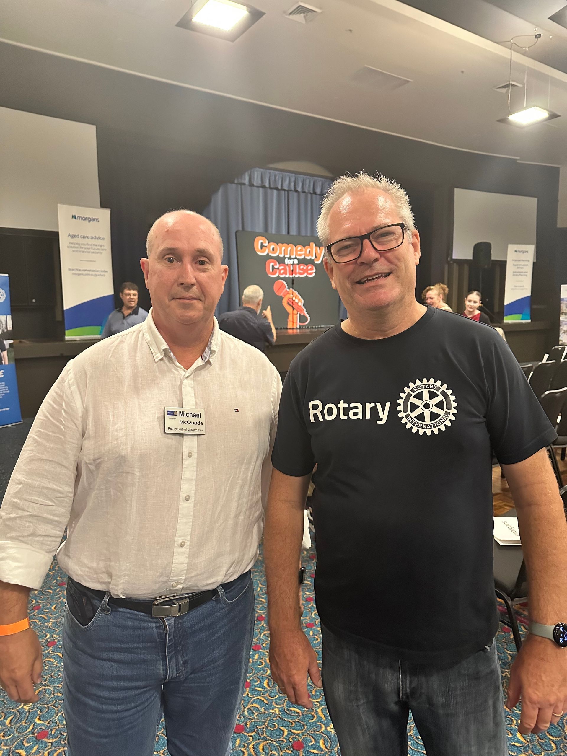 Two men are standing next to each other in a room and one of them is wearing a rotary shirt.