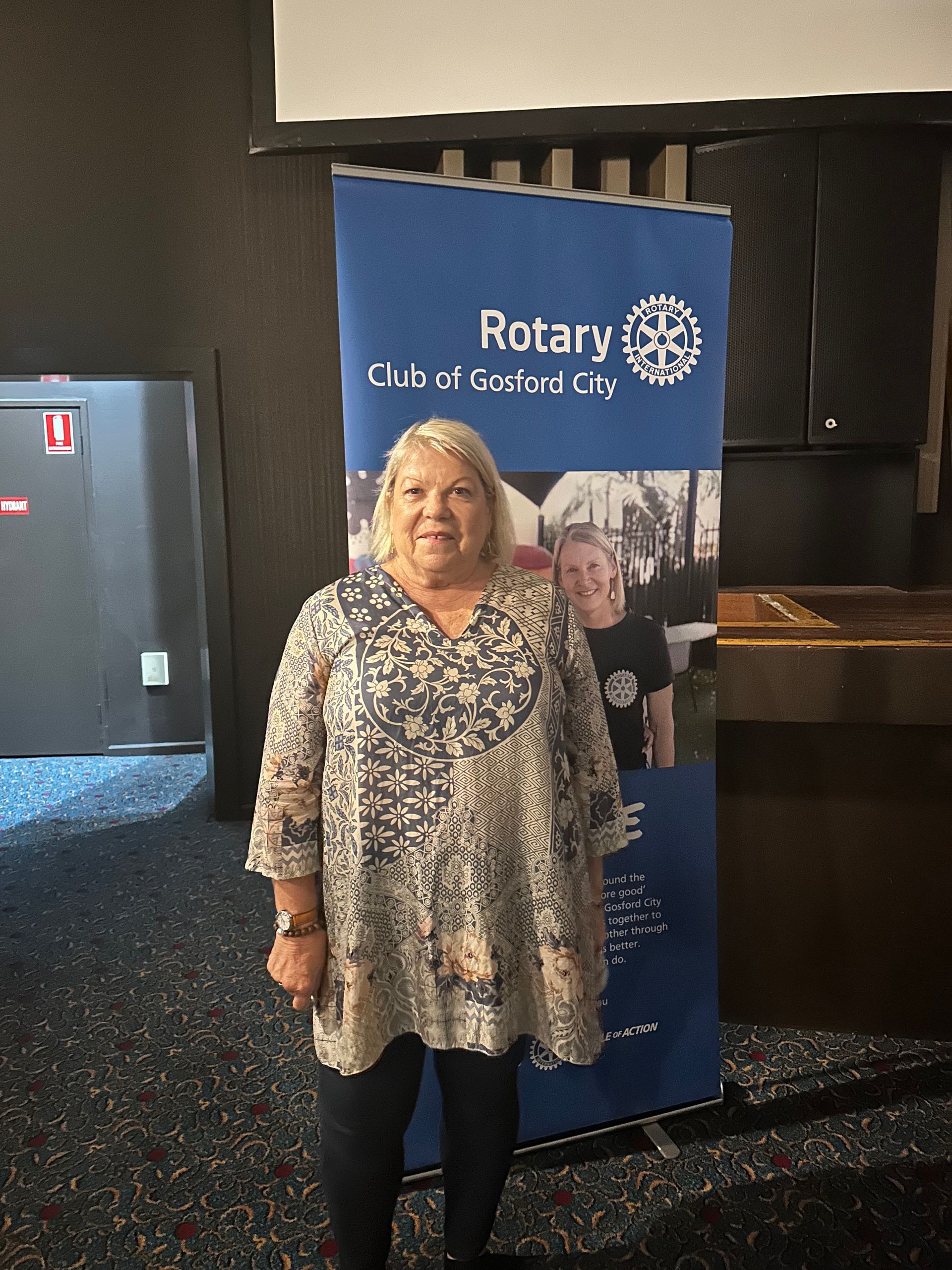 A woman is standing in front of a rotary banner