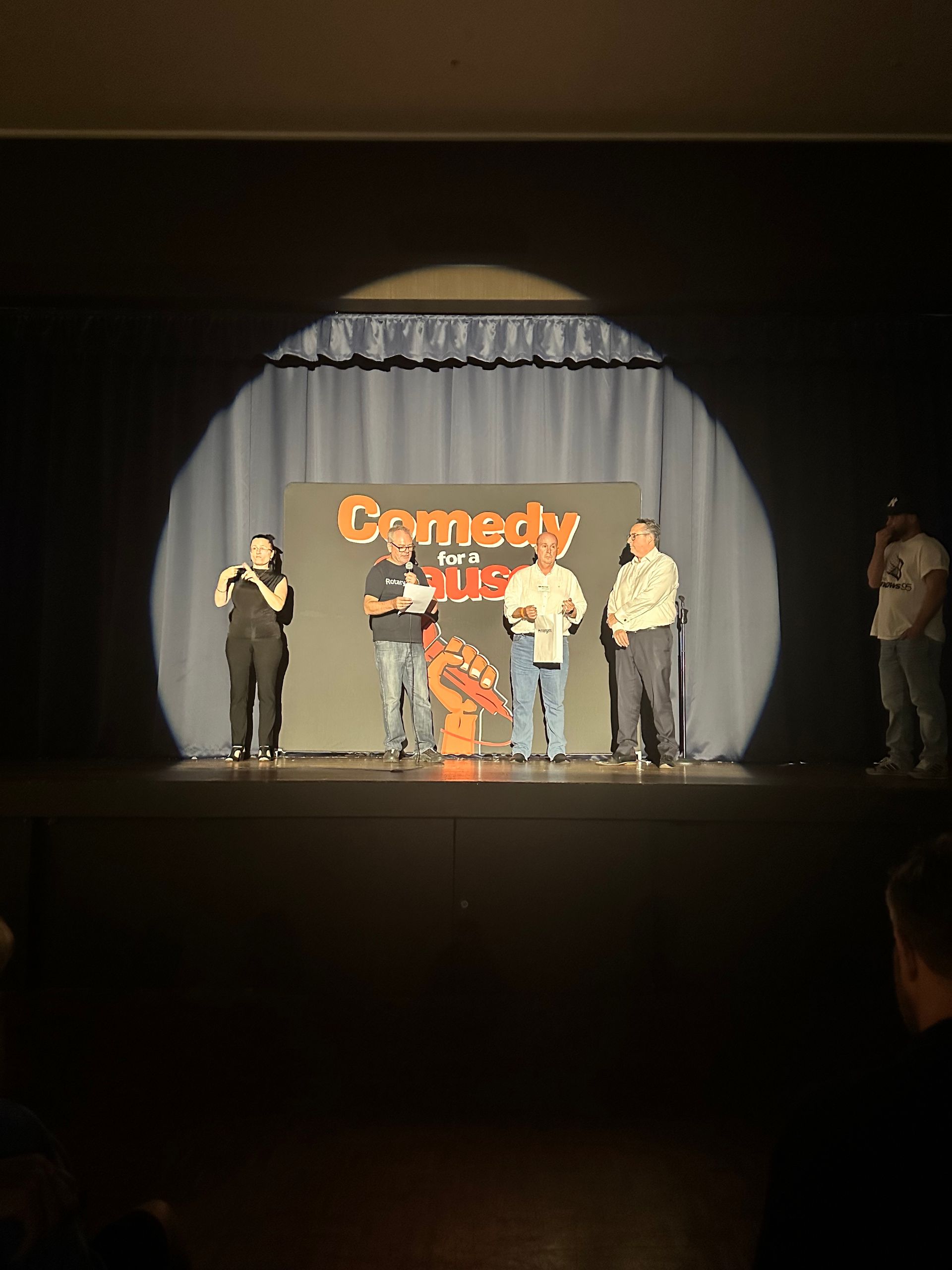 A group of people are standing on a stage in front of a sign that says comedy jam.