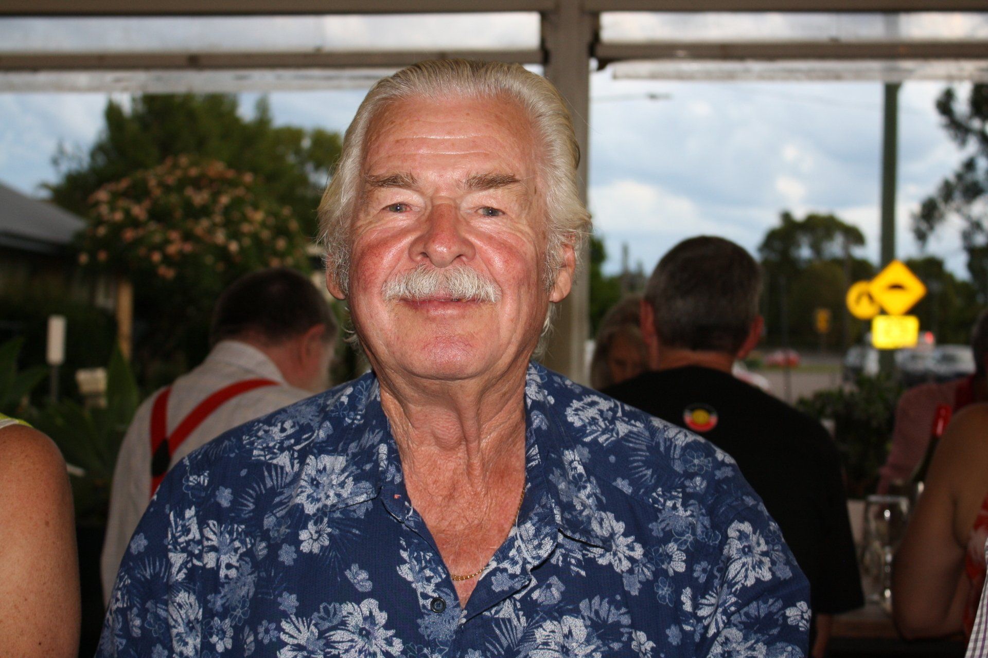 A man with a mustache is wearing a blue shirt with flowers on it