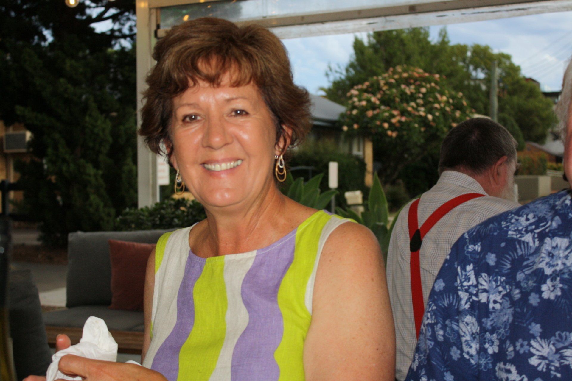 A woman in a purple and green striped dress is smiling while holding a napkin.