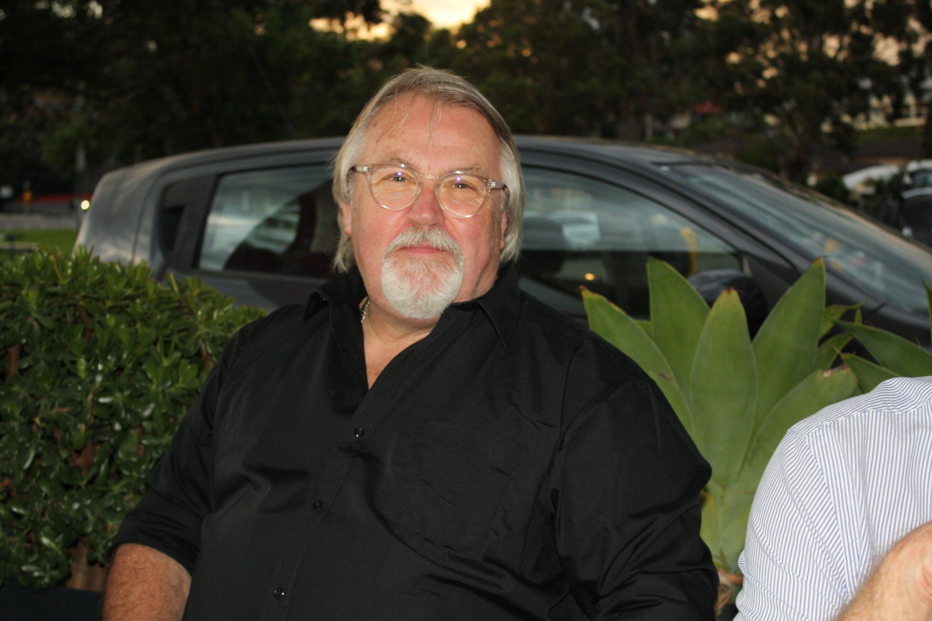 A man with glasses and a beard is sitting in front of a car.