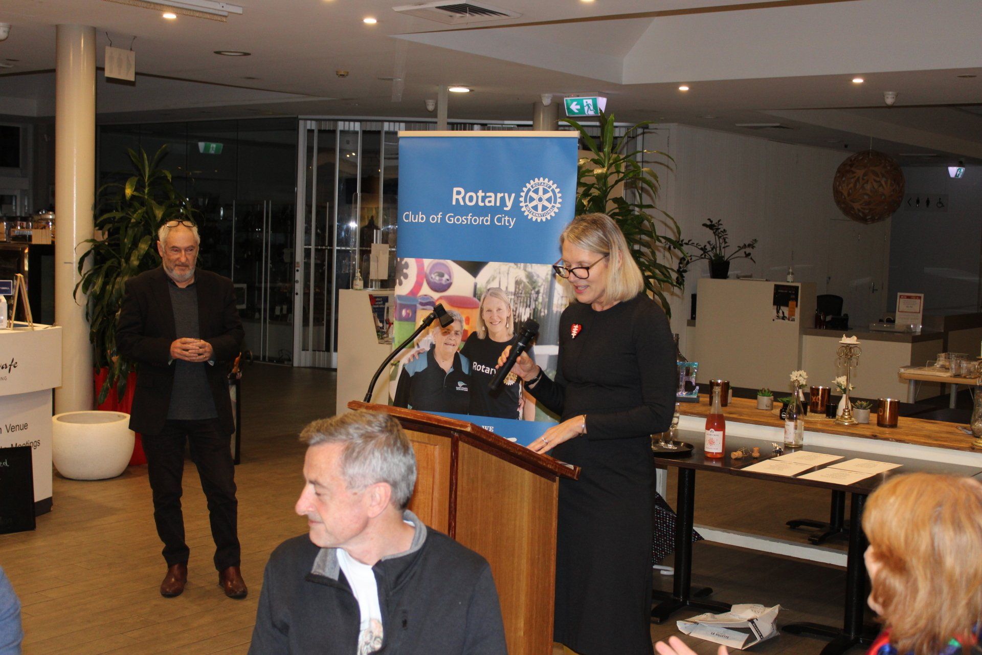 A woman is giving a speech at a podium in front of a sign that says rotary
