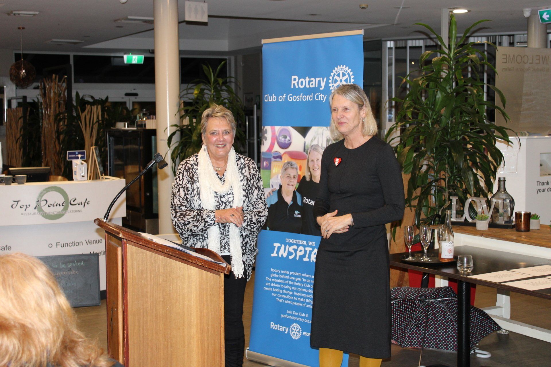 Two women are standing at a podium in front of a sign that says rotary