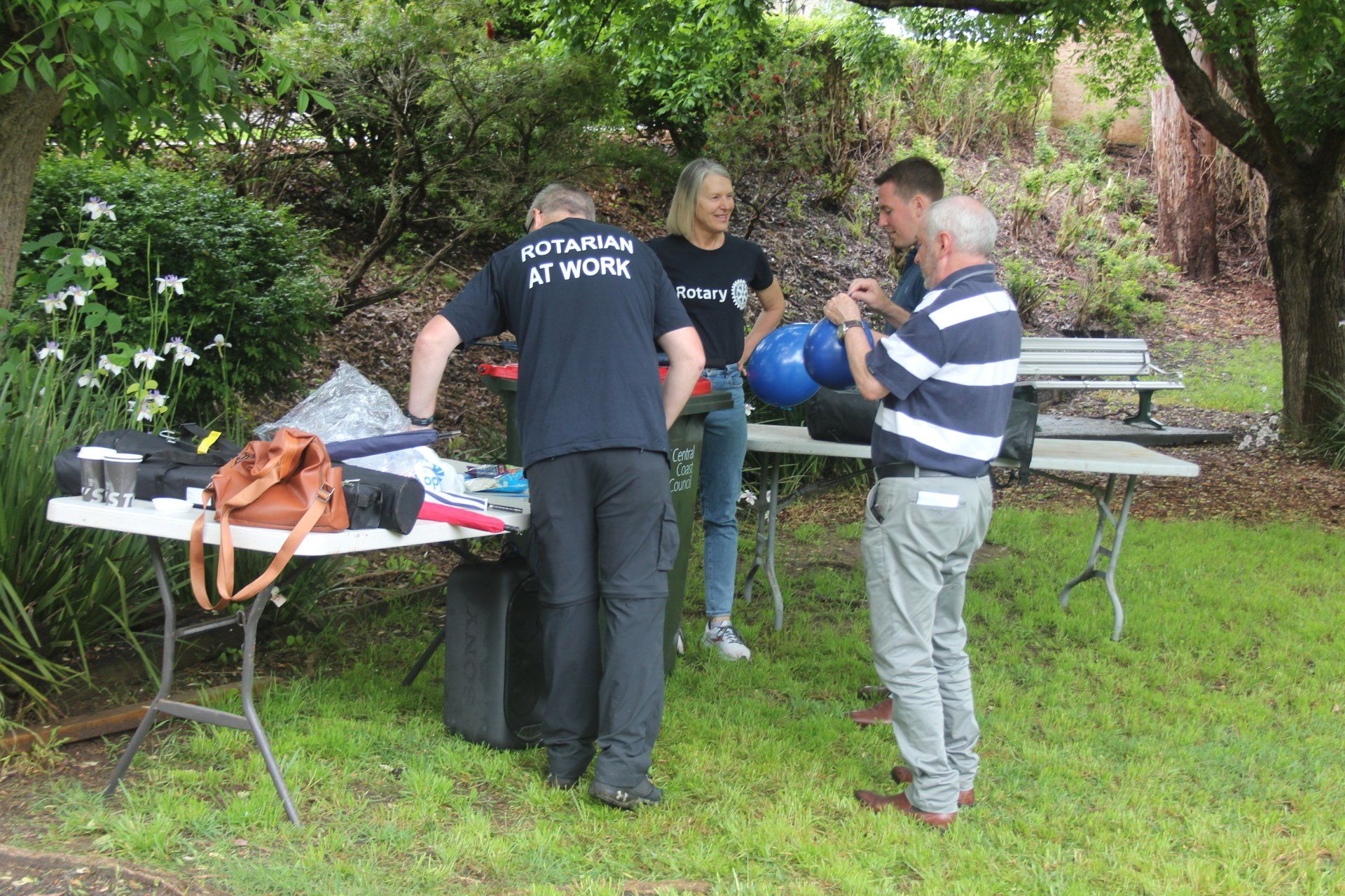 A group of people are standing around a table in a park.