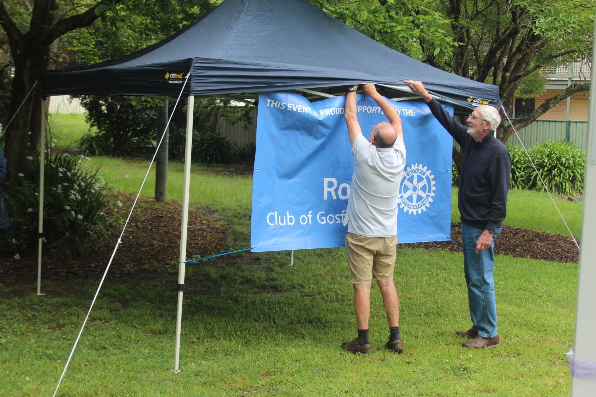 Two men are setting up a canopy with a banner that says rotary club of scotland