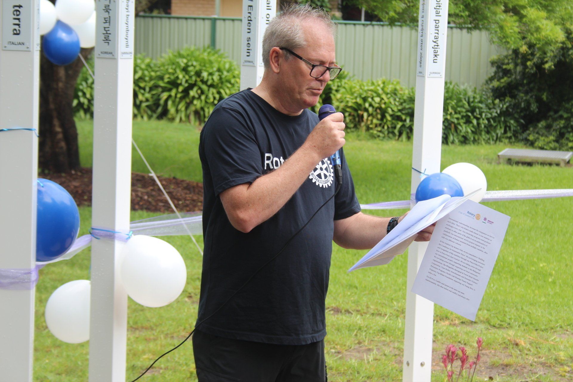 A man is speaking into a microphone while holding a piece of paper.