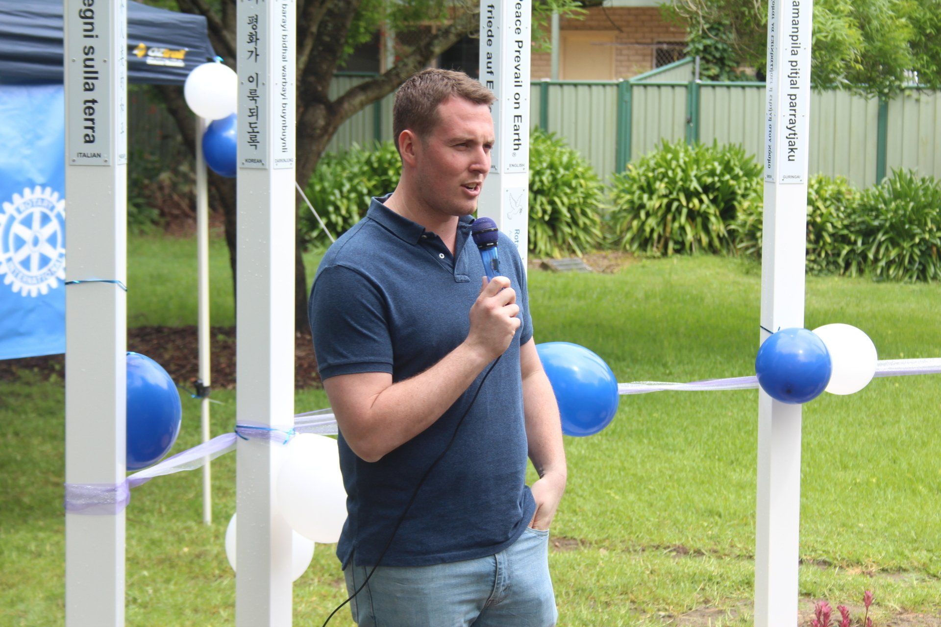 A man in a blue shirt is speaking into a microphone