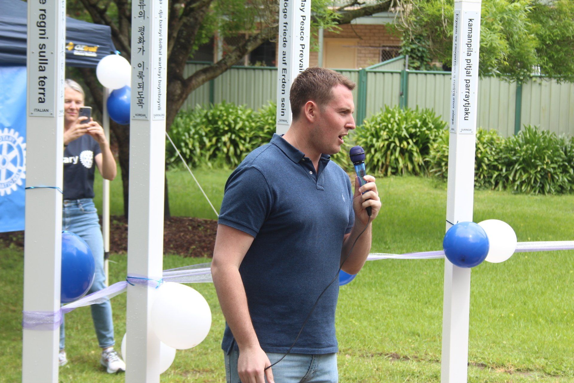 A man in a blue shirt is speaking into a microphone