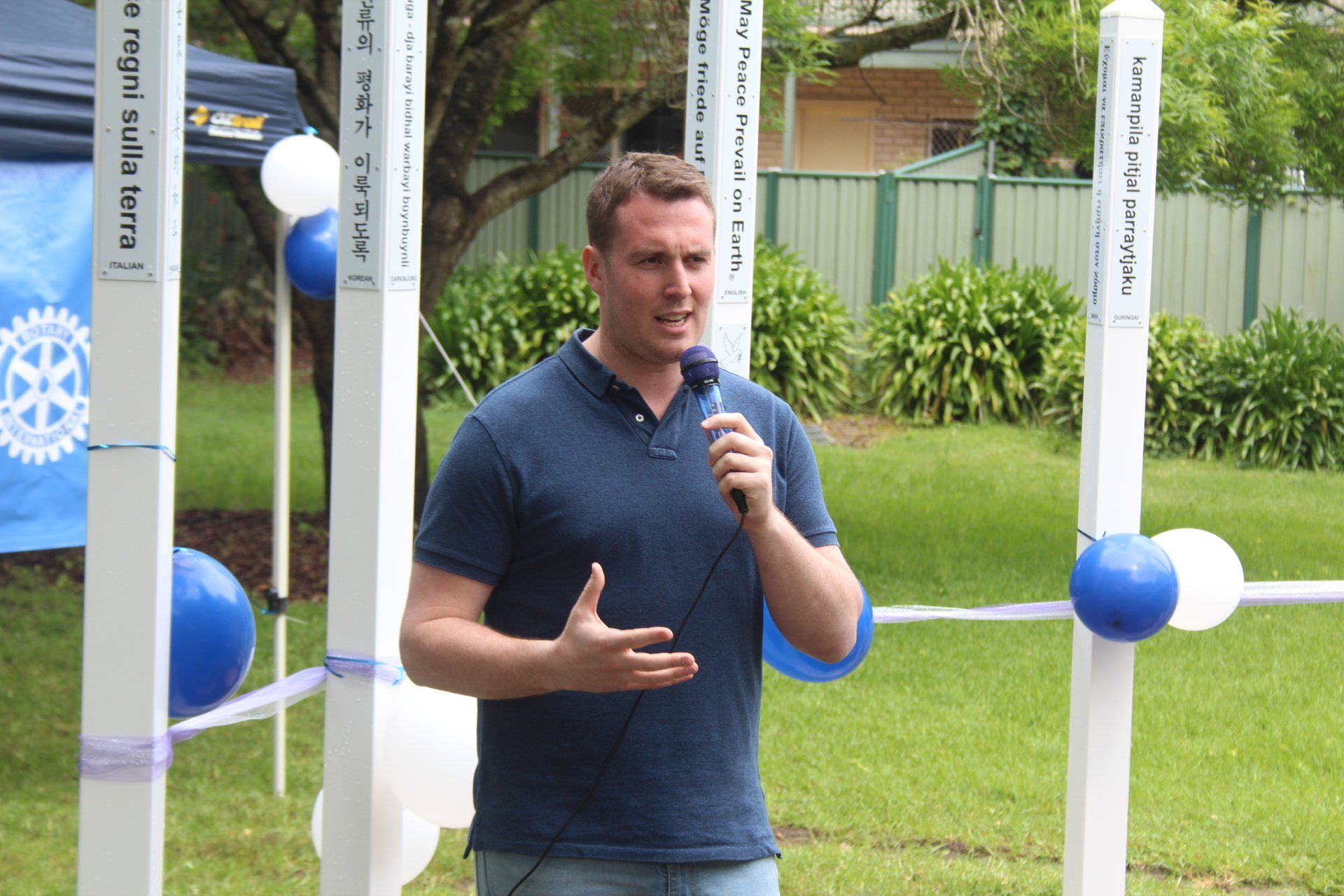 A man in a blue shirt is speaking into a microphone